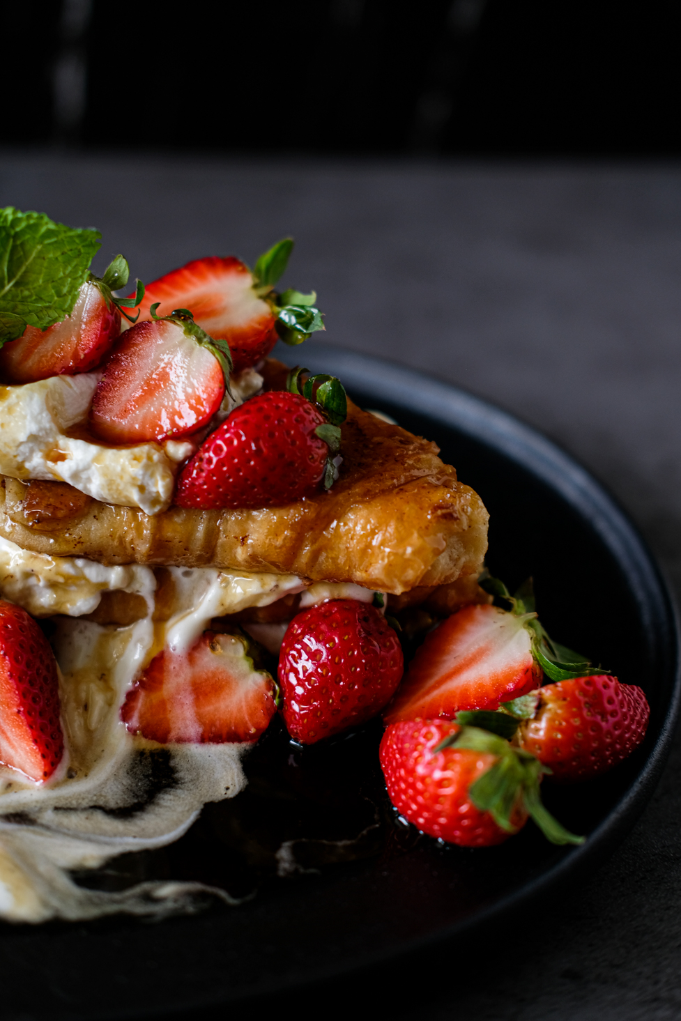 Close-up of a dessert with strawberries, cream, and a pastry on a black plate.