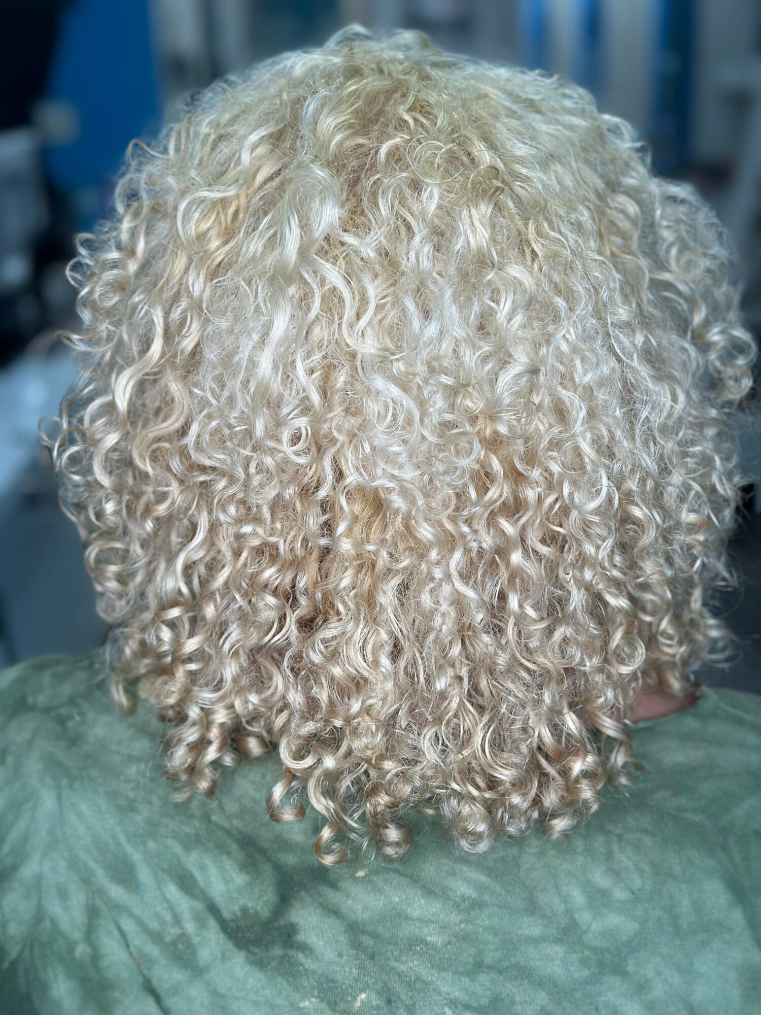 Back of a person with curly, platinum blonde hair, in a setting with blue and white background elements.