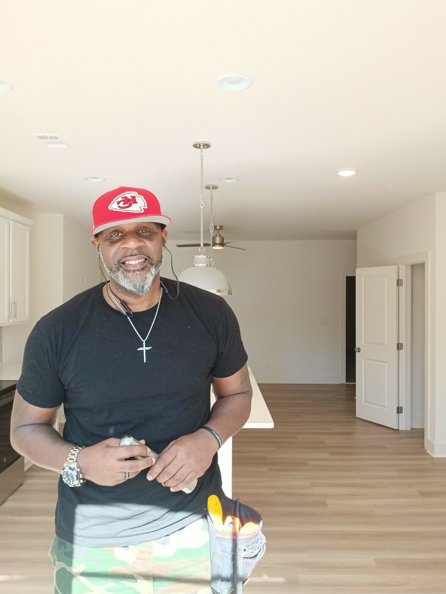 Man wearing a red cap, black shirt, and glasses, standing in a room with white walls and wooden floor.