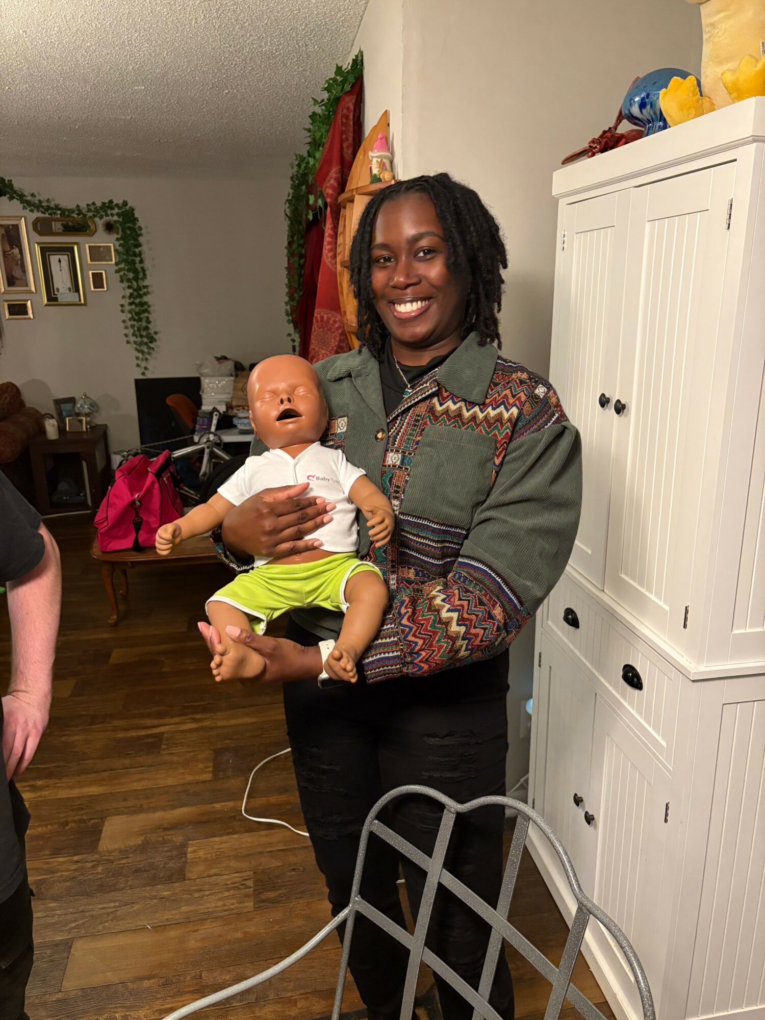 Woman holding a baby in a room with white cabinets and wooden floor, smiling at the camera.