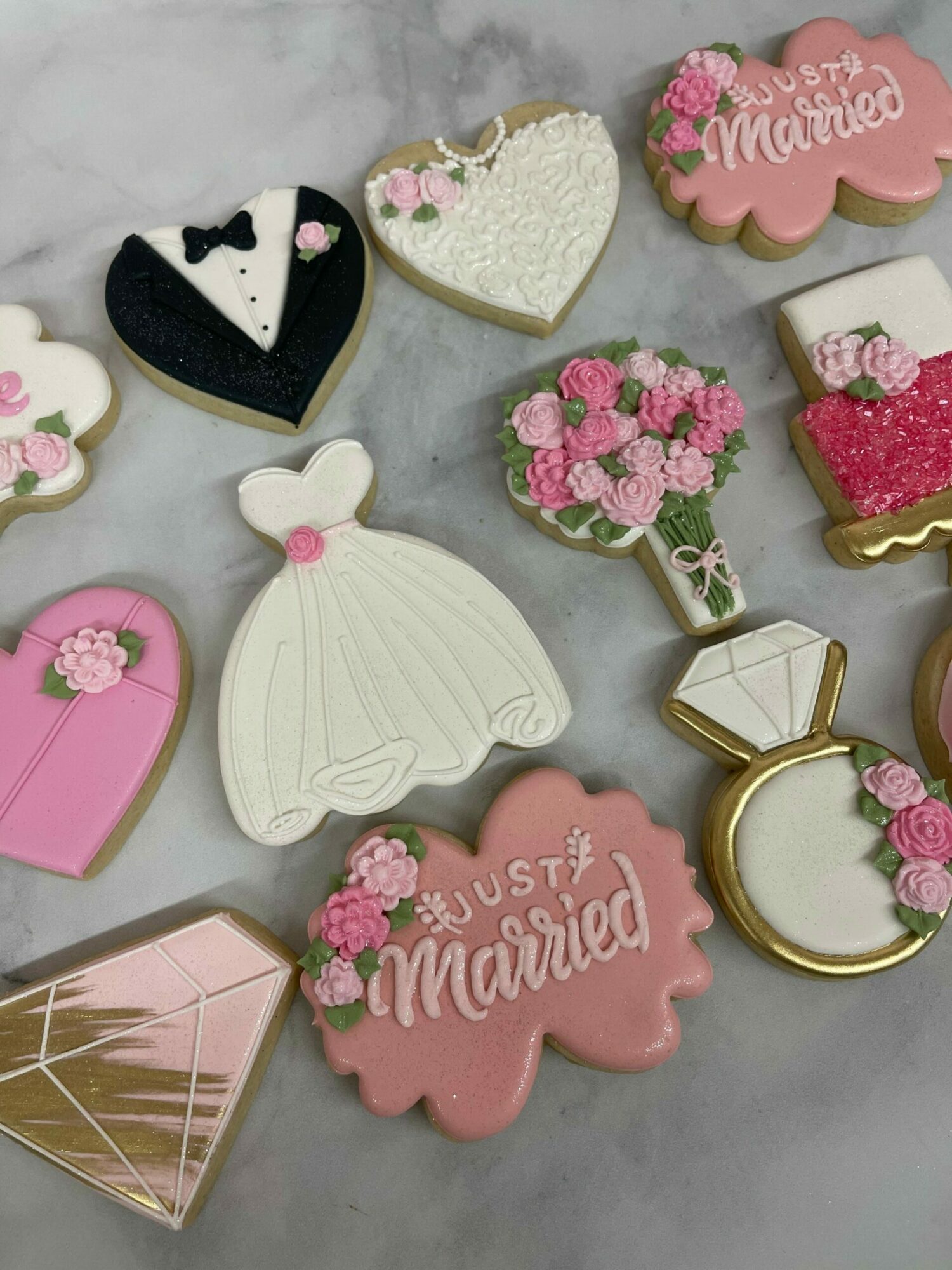 Assorted decorated cookies and jewelry on a gray surface, including pink, white, and black cookies with floral and butterfly designs.