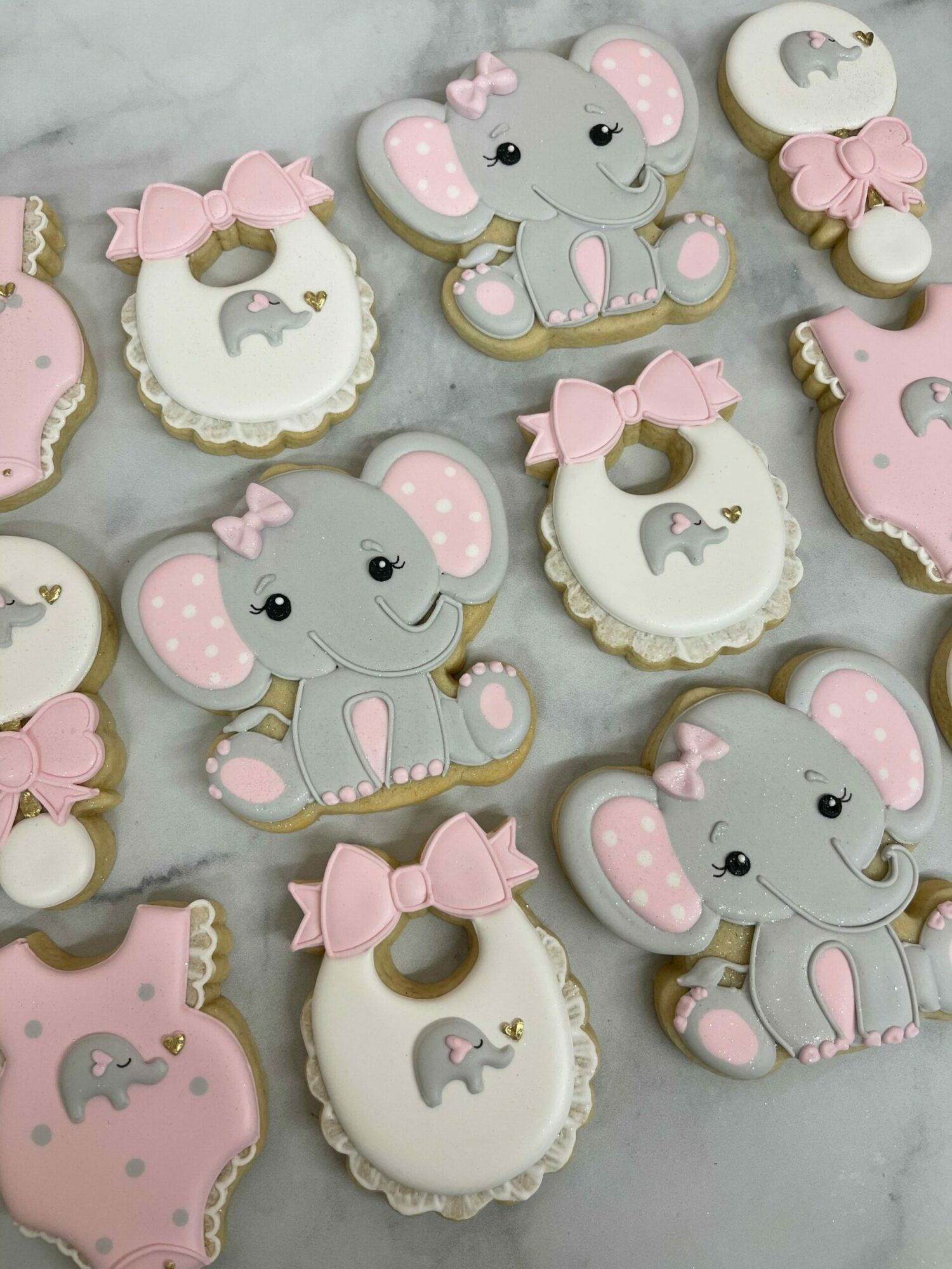 Assorted decorated cookies with pink, gray, and white colors, featuring mouse and baby carriage designs, on a light surface.