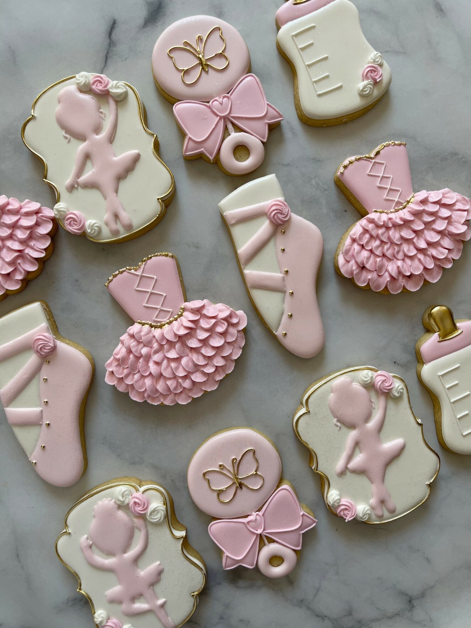 Decorative cookies with ballet, bows, and pink ruffles on a marble surface.
