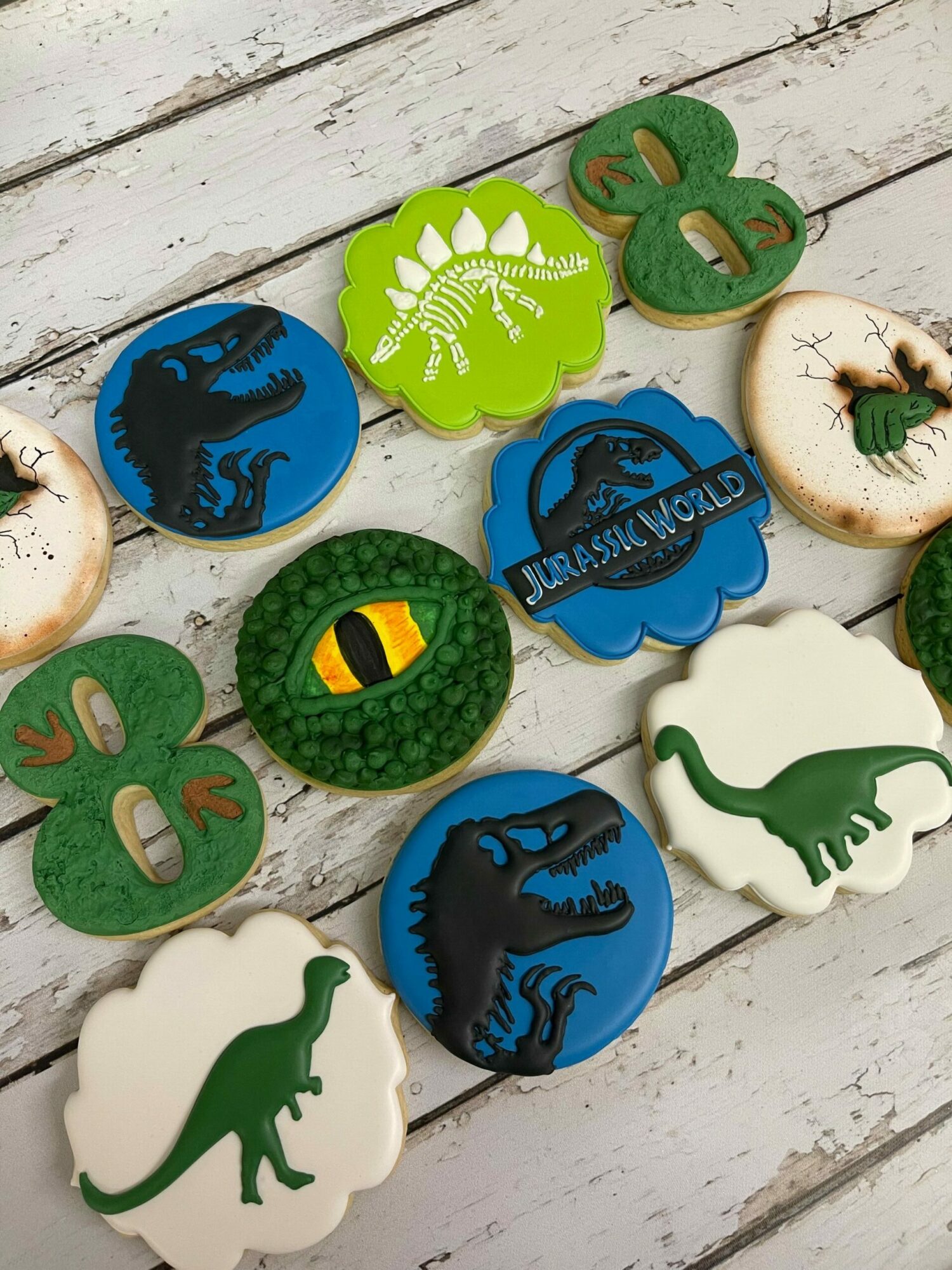 Collection of dinosaur-themed cookies with various colors and designs on a wooden surface.