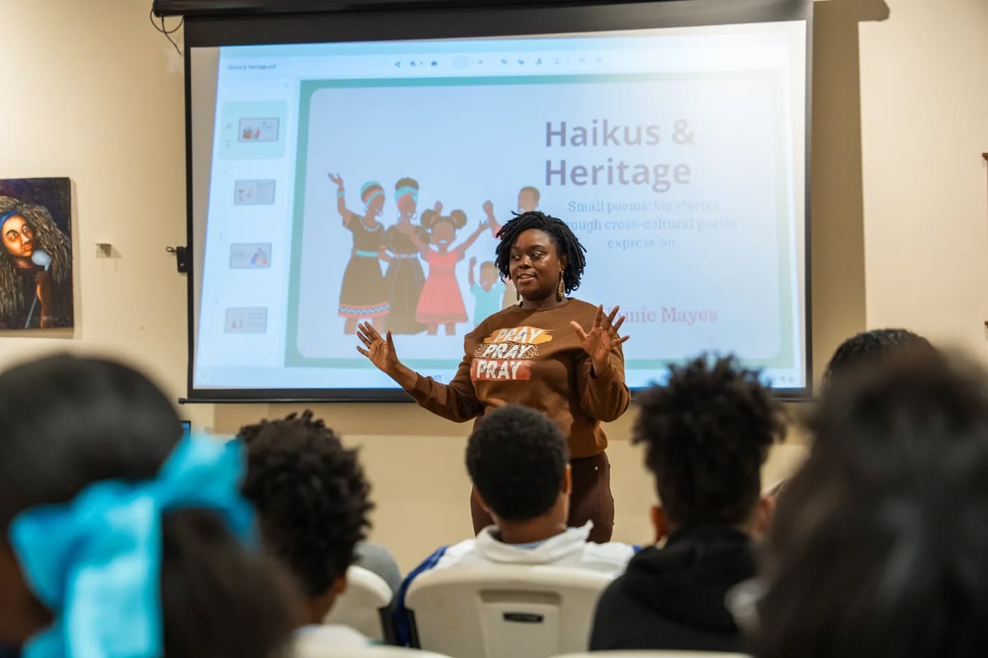 Woman giving a presentation to a group of children in a classroom, with a slide titled 'Haikus & Heritage' behind her.