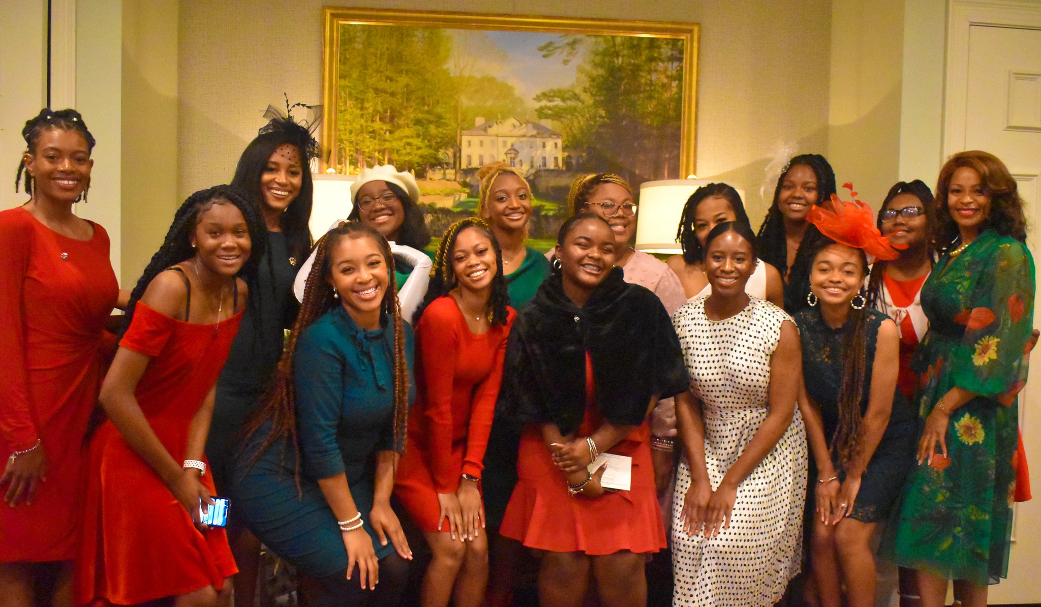 Group of women smiling and posing indoors in front of a painting, dressed in colorful clothing.