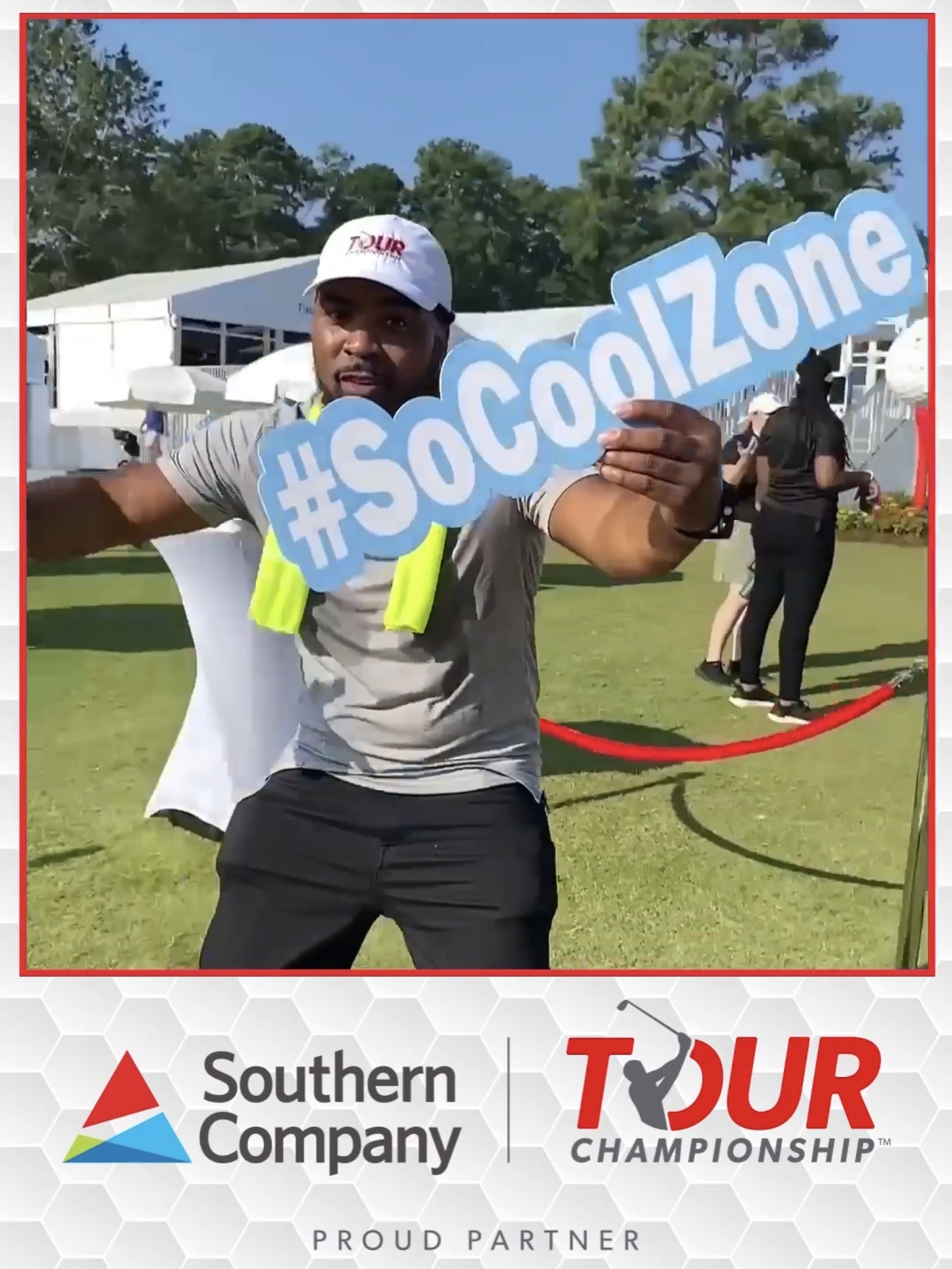 Person holding a blue sign with hashtag #SoCoolZone outdoors, with trees and people in background, at a golf event.