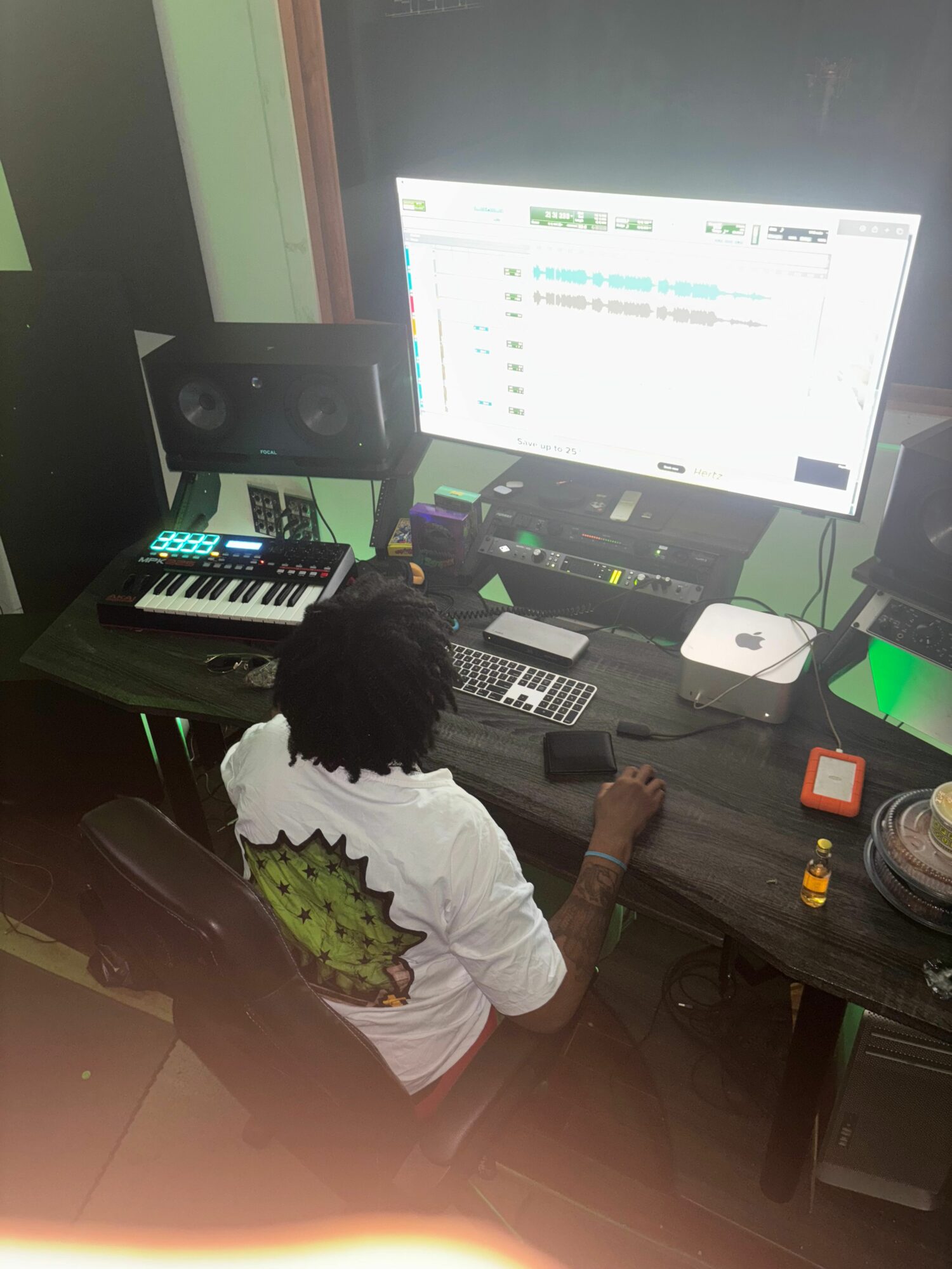 Person working at a desk with a computer monitor, keyboard, and music production equipment.