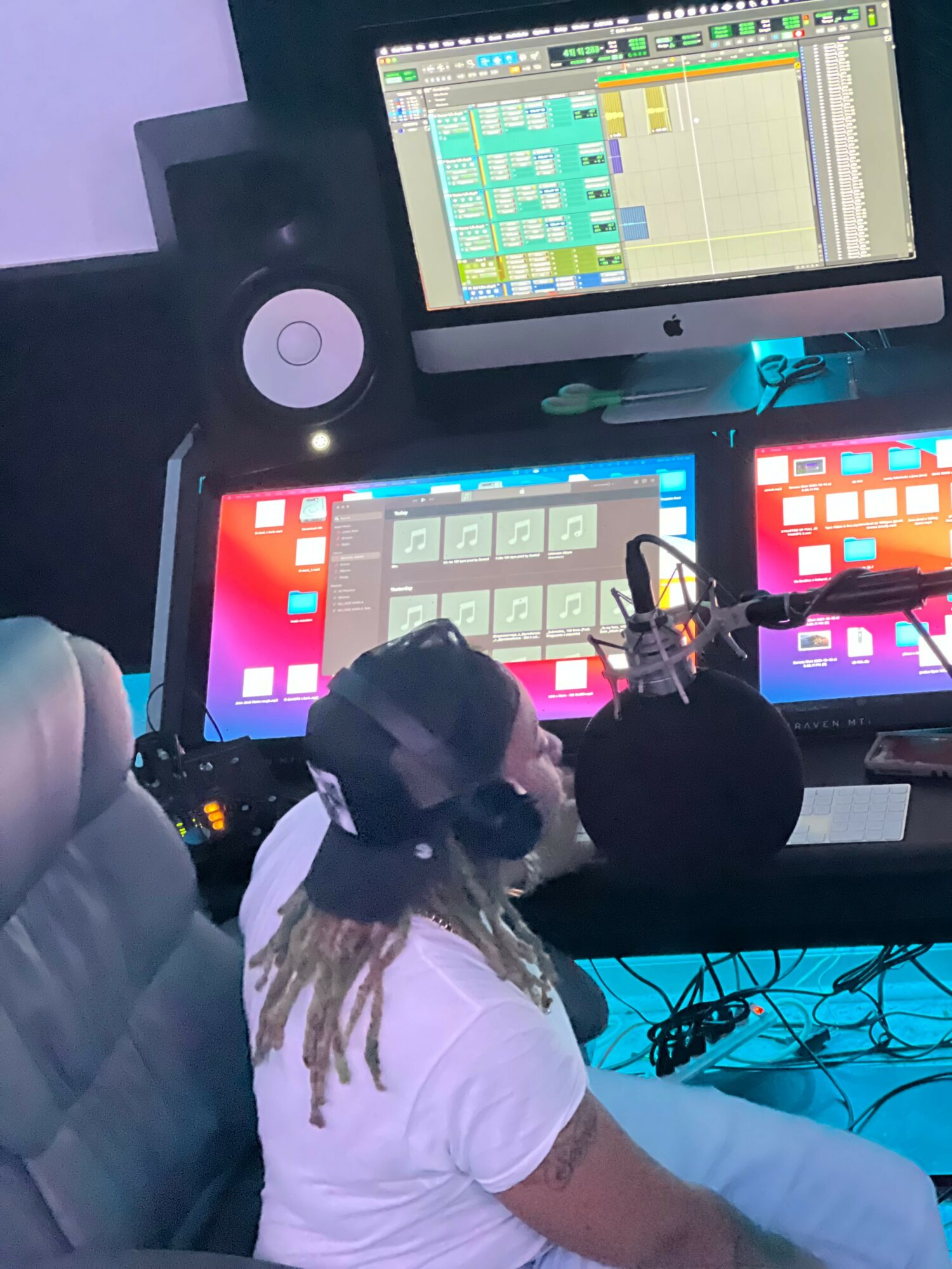 Person with dreadlocks wearing headphones working with music production equipment in a studio.