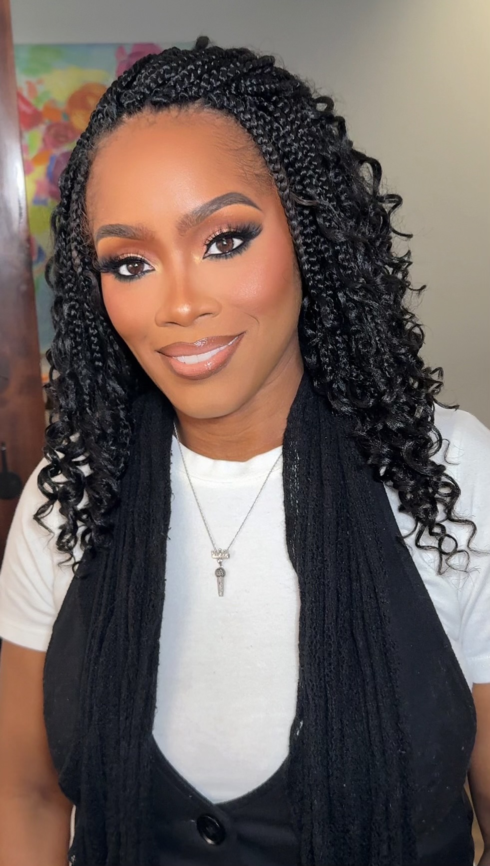 Young woman with curly hair, makeup, and a necklace, smiling at the camera.
