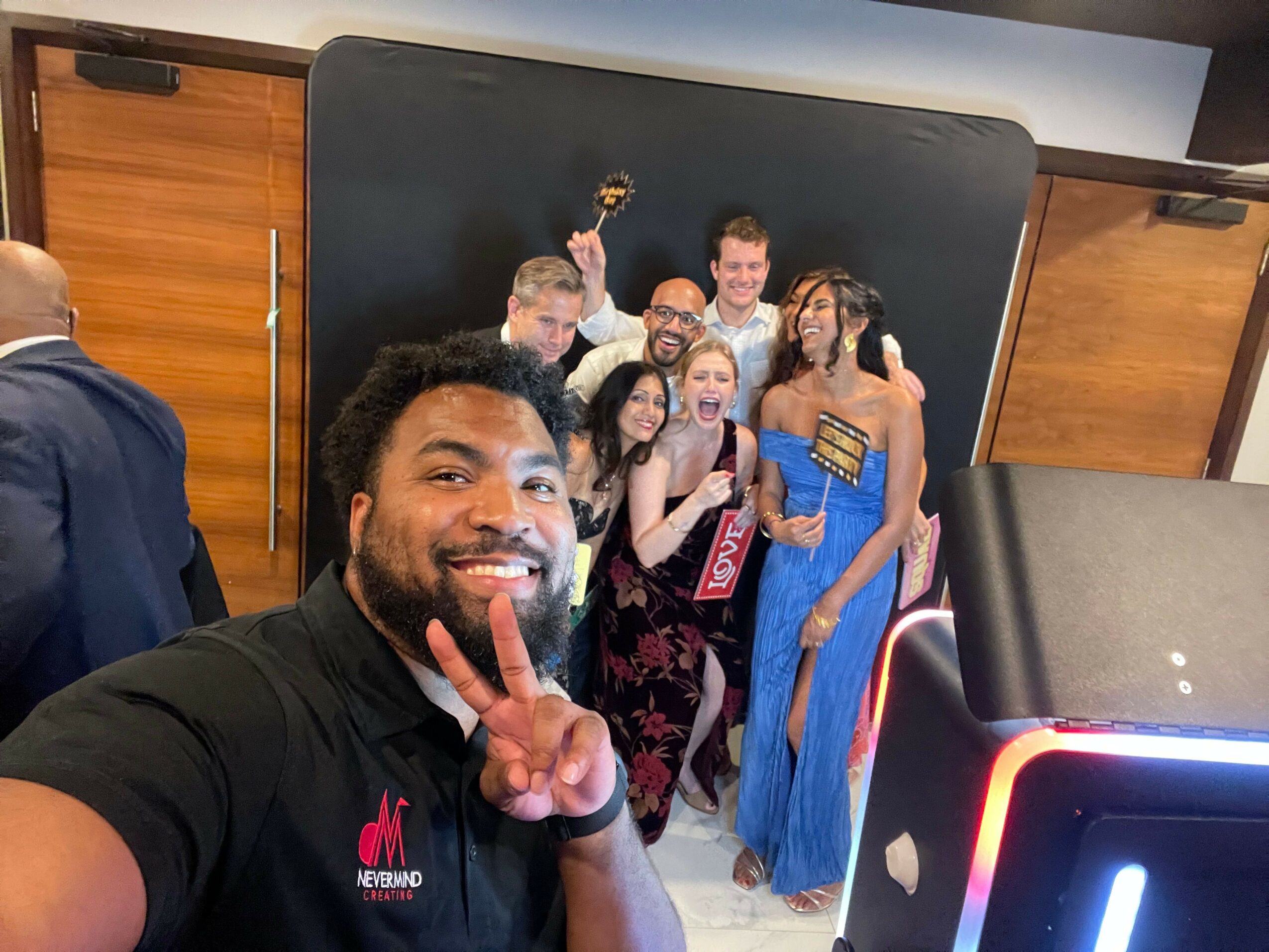 Group of people posing indoors, some making peace signs, with a man in the foreground smiling and holding up a peace sign.