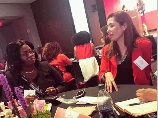 Two women seated at a table engaged in conversation, with a floral centerpiece and various items on the table.