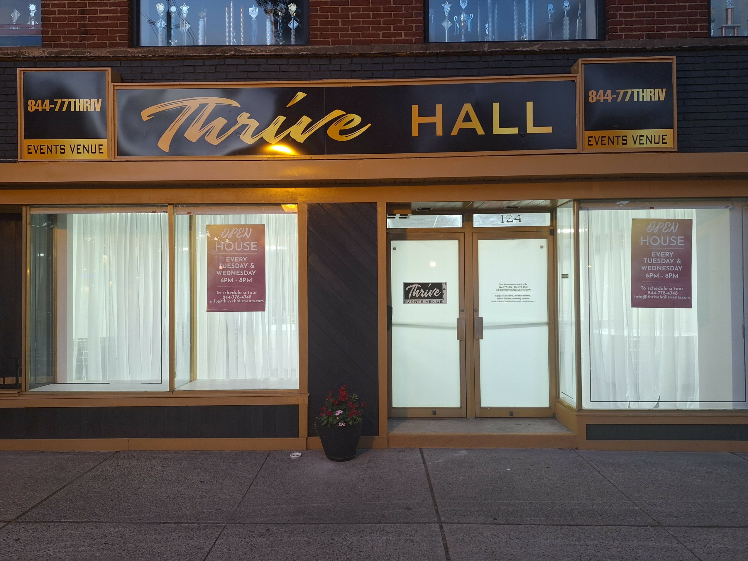 Storefront with large windows, double glass doors, and a sign reading 'Trine Hall' above the entrance.