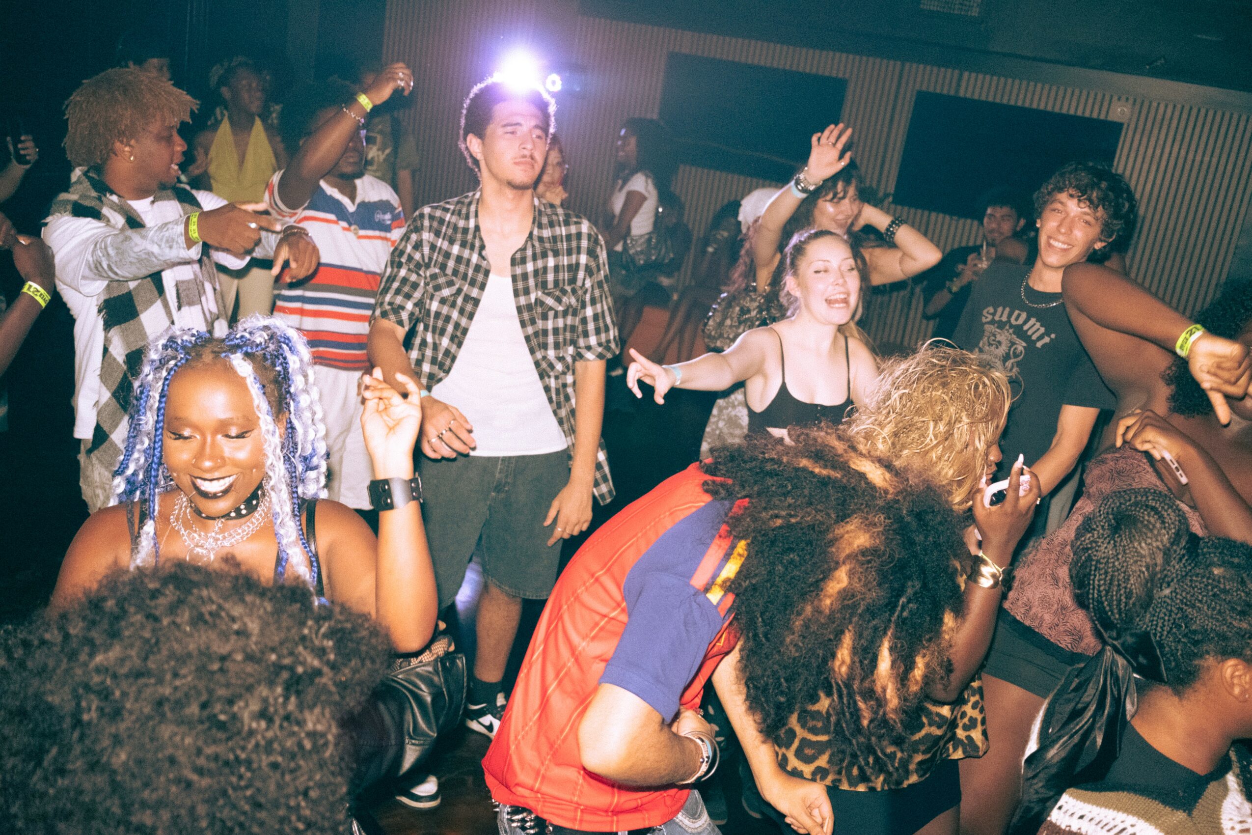 Group of young people dancing and enjoying a party in a dimly lit room with colorful lighting.