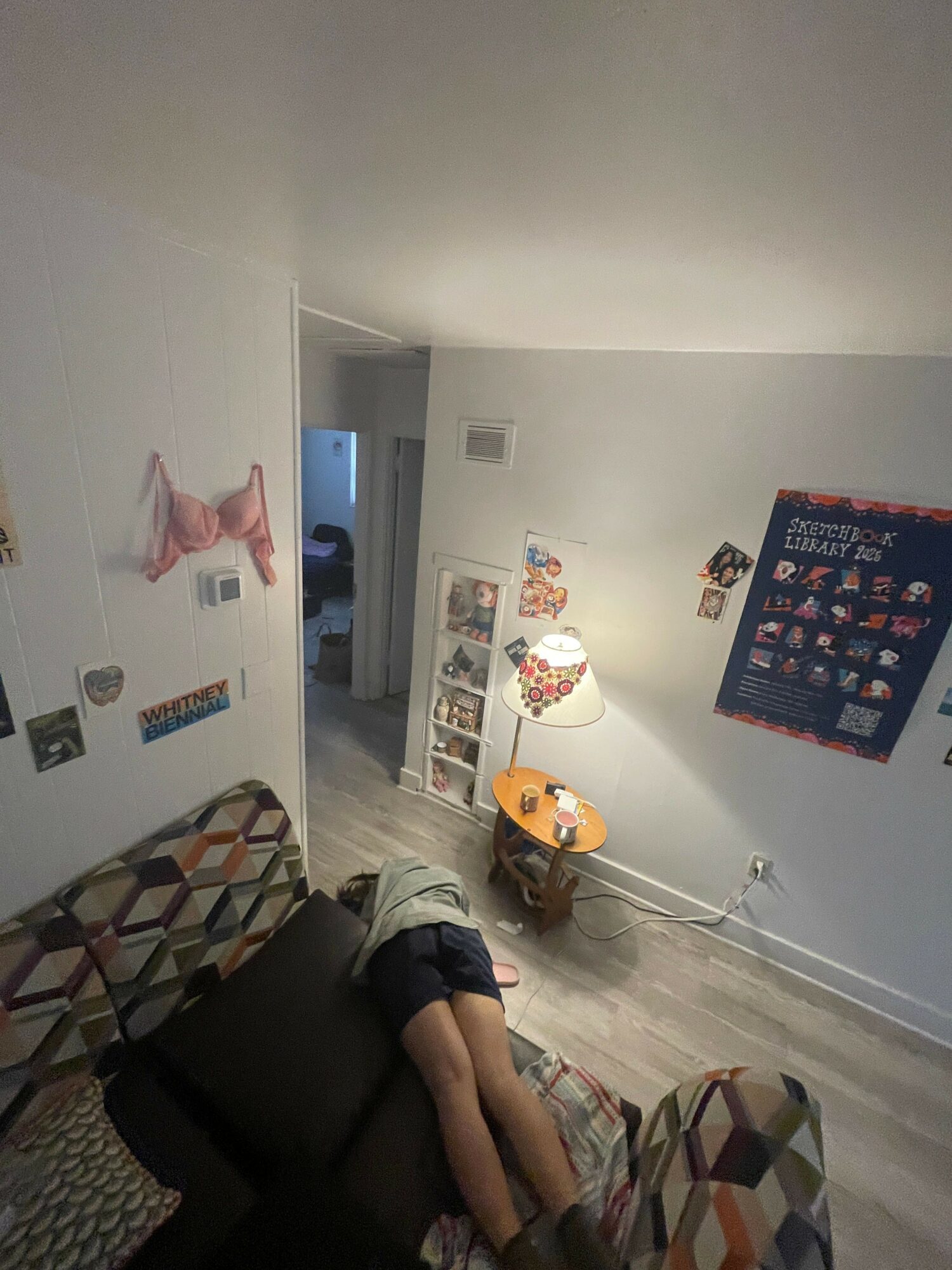 Child lying on a couch in a living room with a patterned armchair, lamp, and wall decorations.