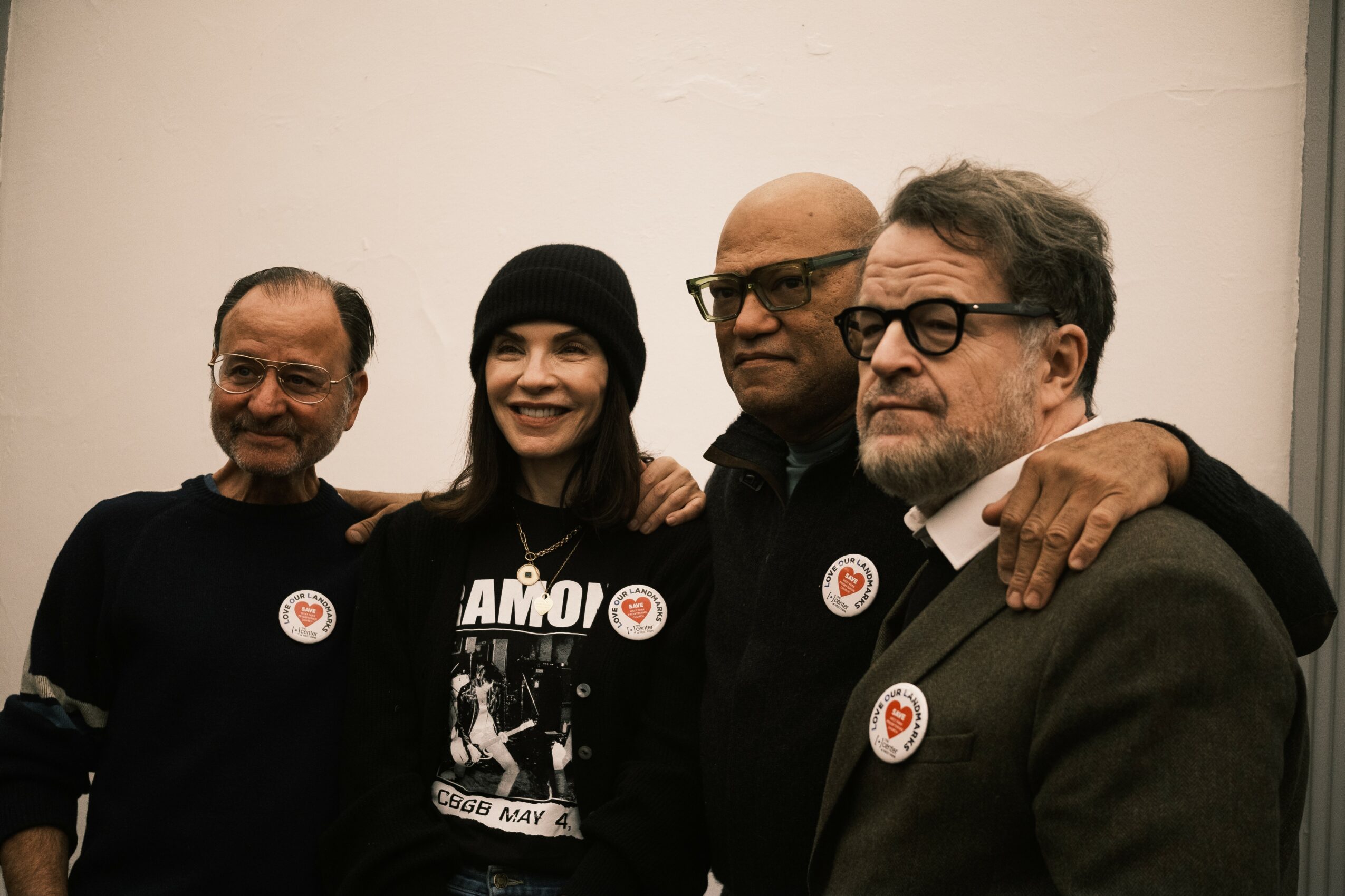 Four people standing together, smiling, with a plain light-colored background.