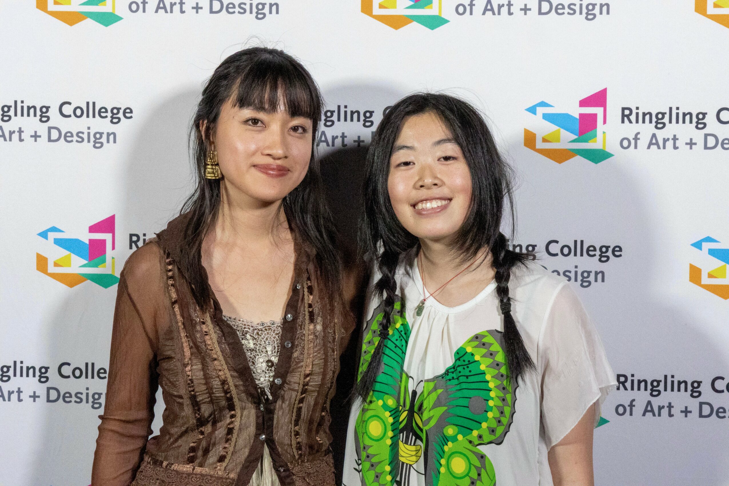 Two women standing together in front of a backdrop with college logos, smiling at the camera.