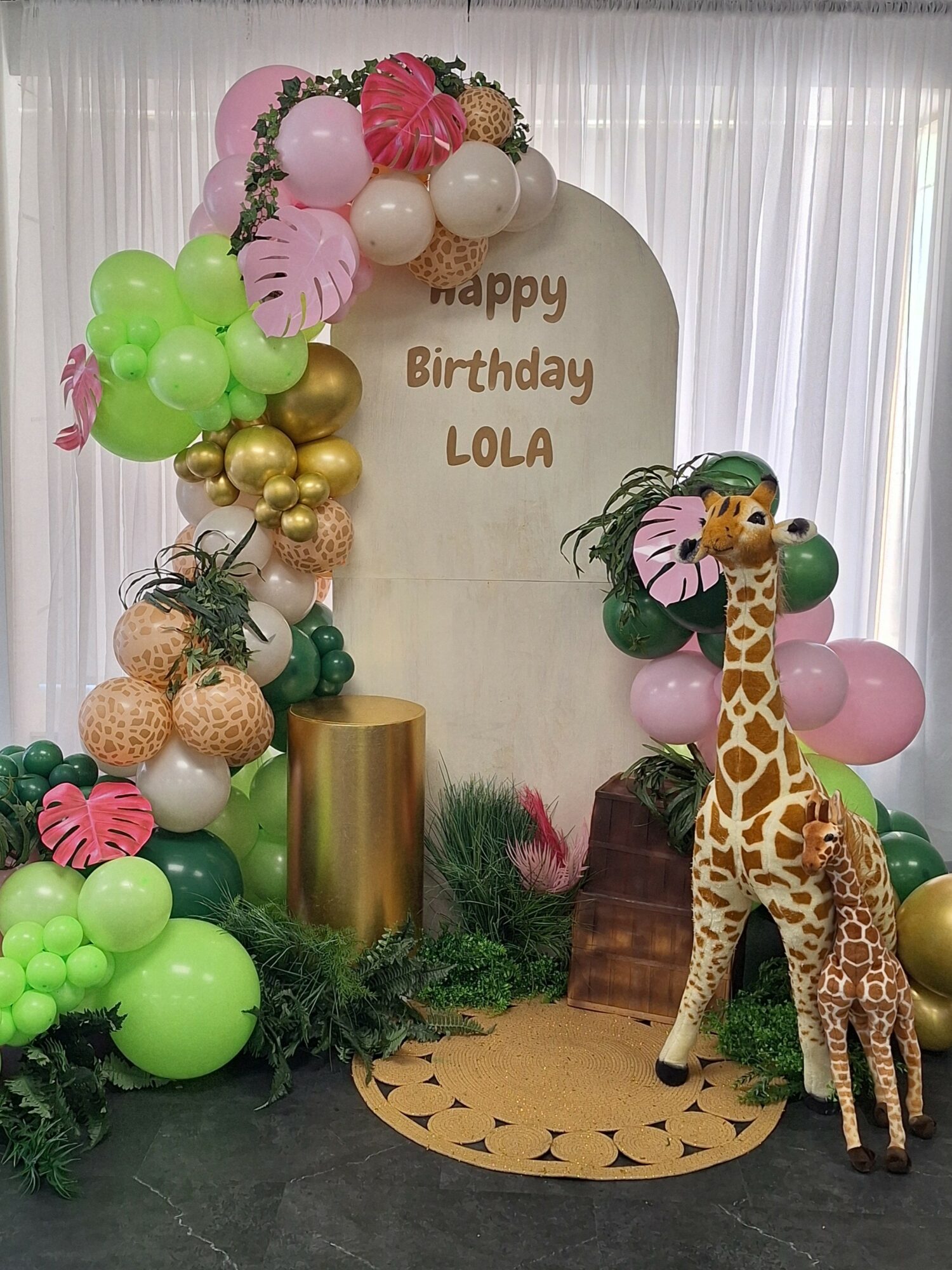 Decorative birthday setup with balloons, a giraffe plush, and a backdrop reading 'happy Birthday LOLA'.
