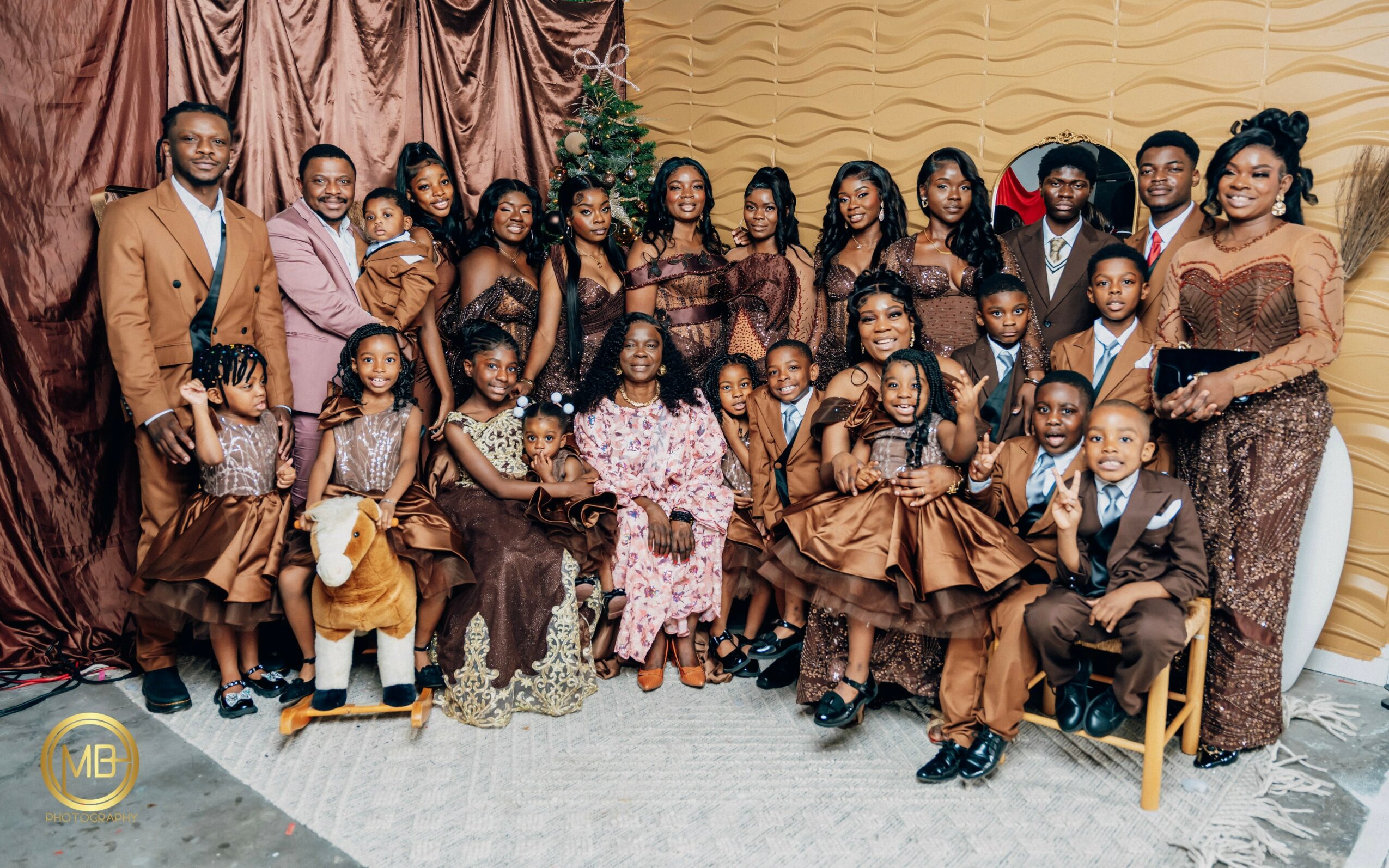 Group of children and adults dressed in formal attire, posing indoors with a brown curtain backdrop.
