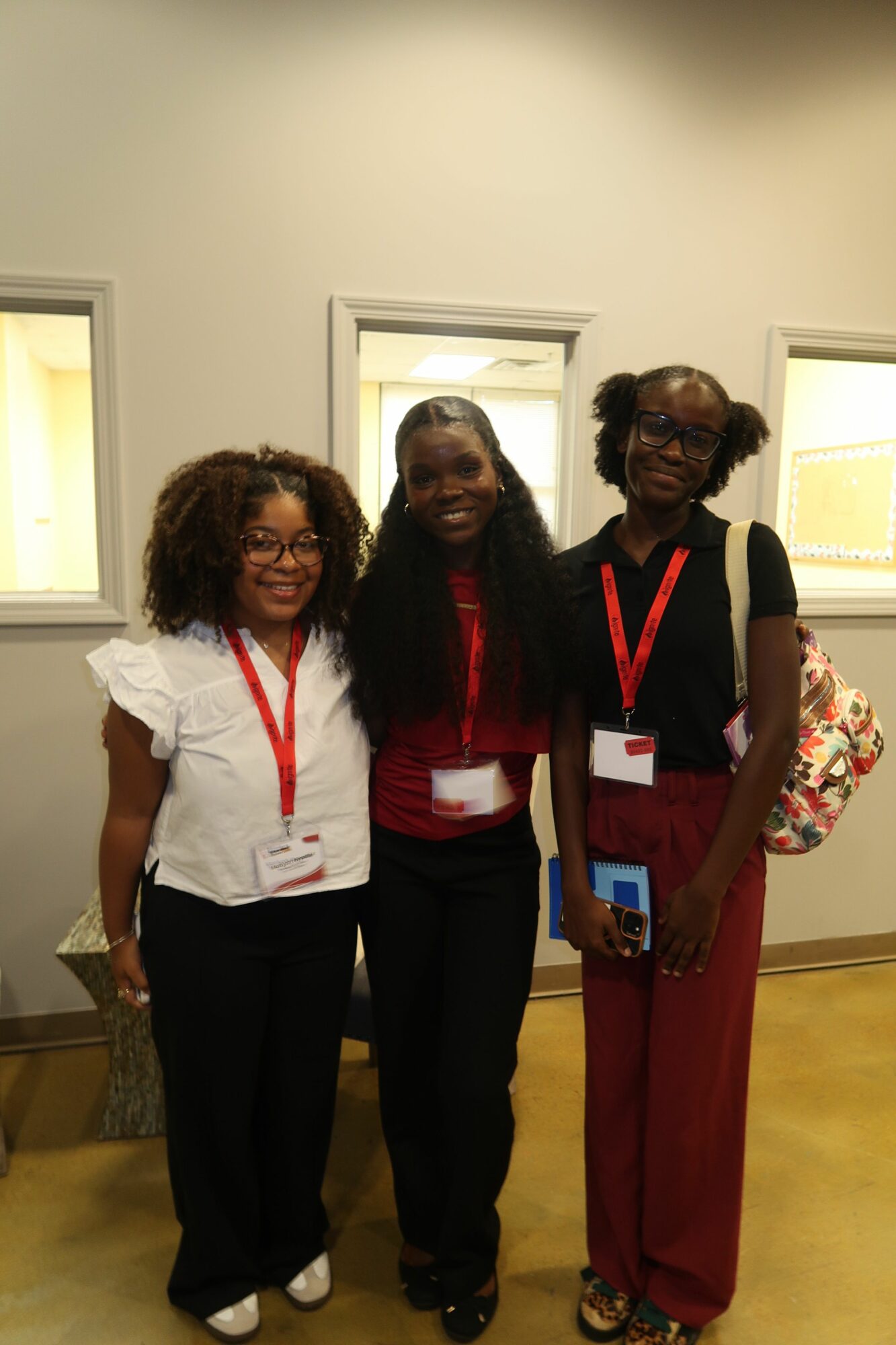 Three women standing together indoors, smiling, with name tags and lanyards, in front of a white wall.