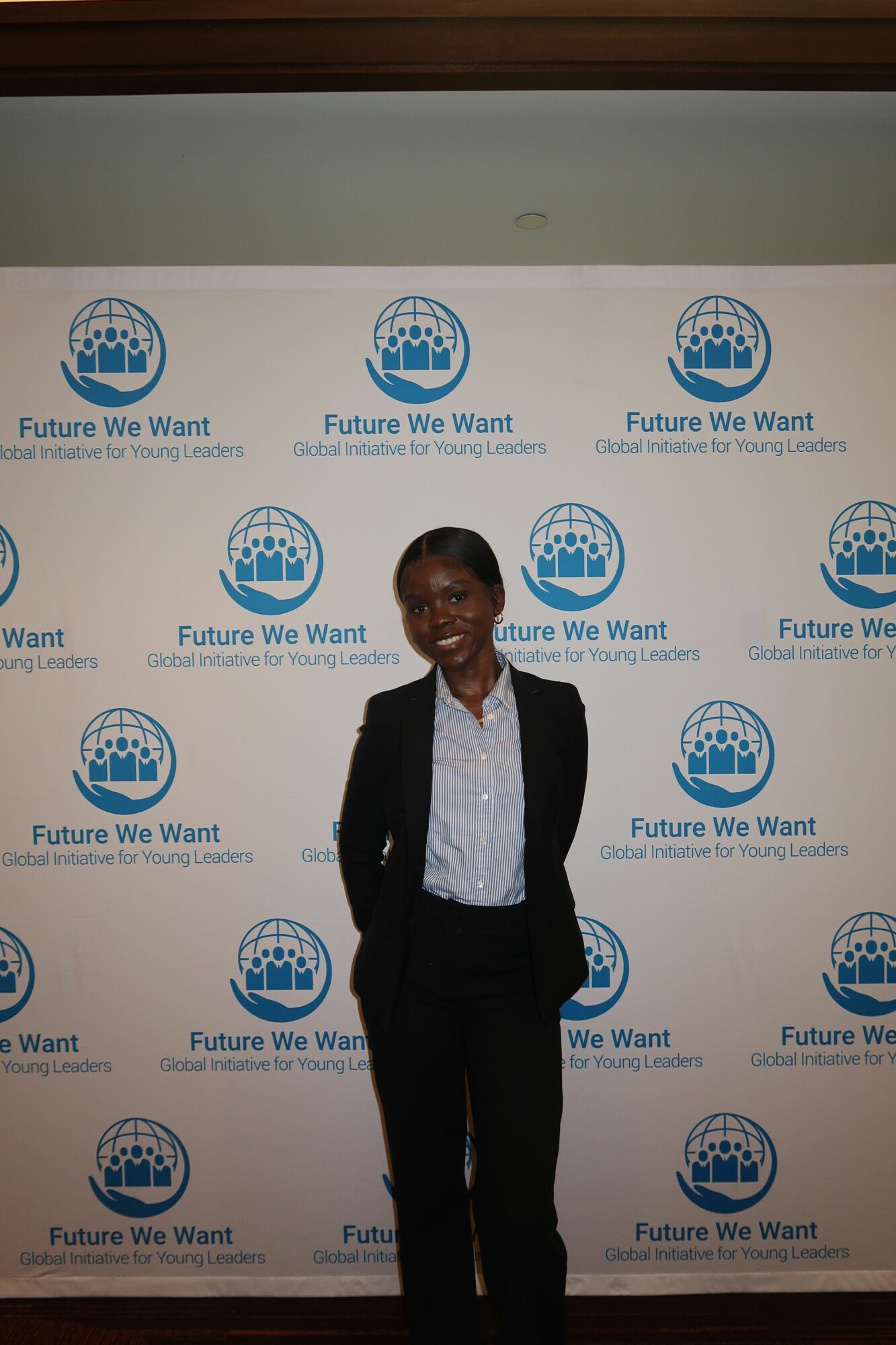 Man in a suit standing in front of a backdrop with logos and text, smiling, indoors.
