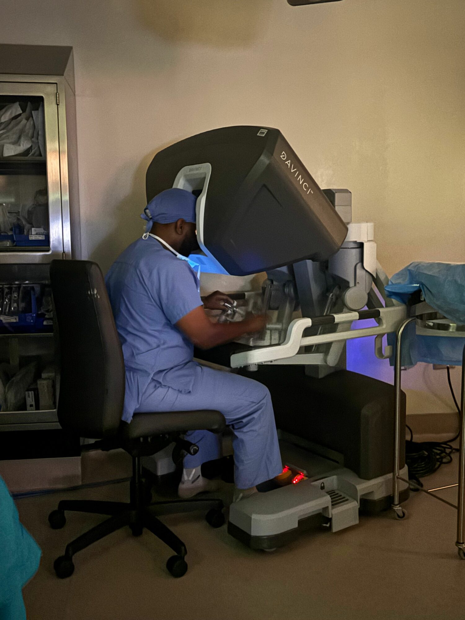 Person in blue scrubs and mask using a medical imaging machine in a clinical setting.