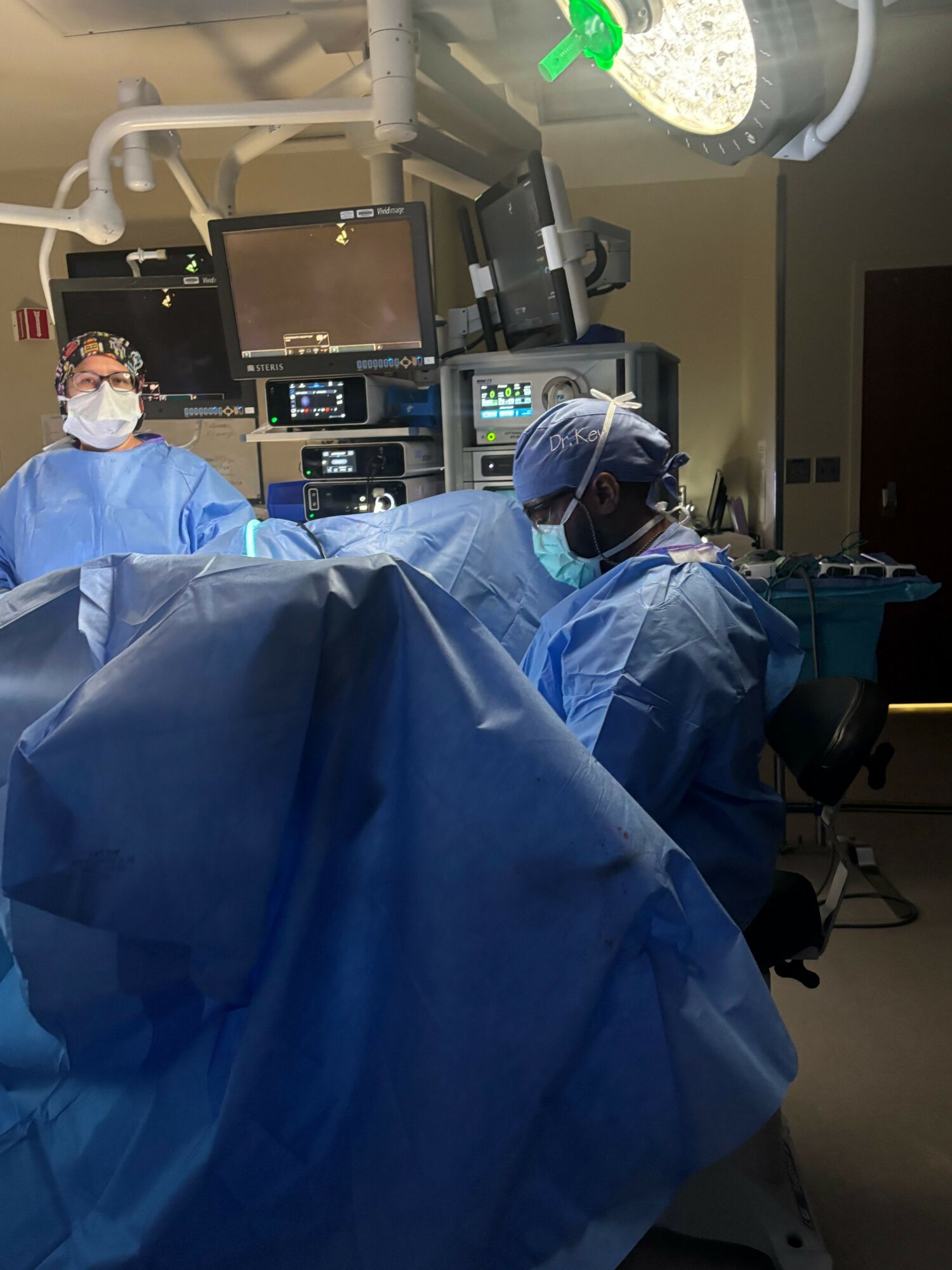 Medical professional in surgical gown and mask operating in an operating room with medical equipment.