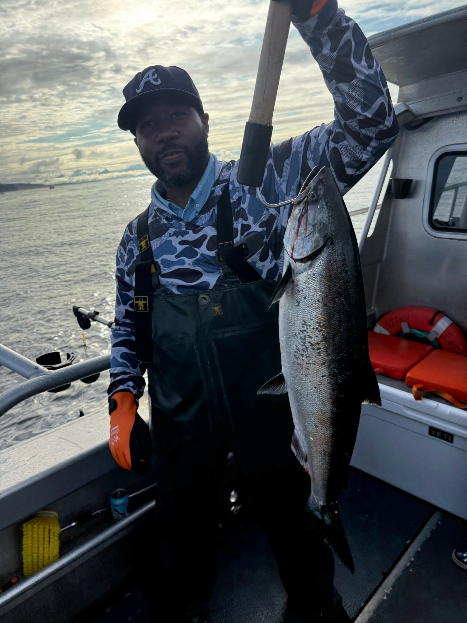 Person holding a large fish on a boat with water and sky in the background.