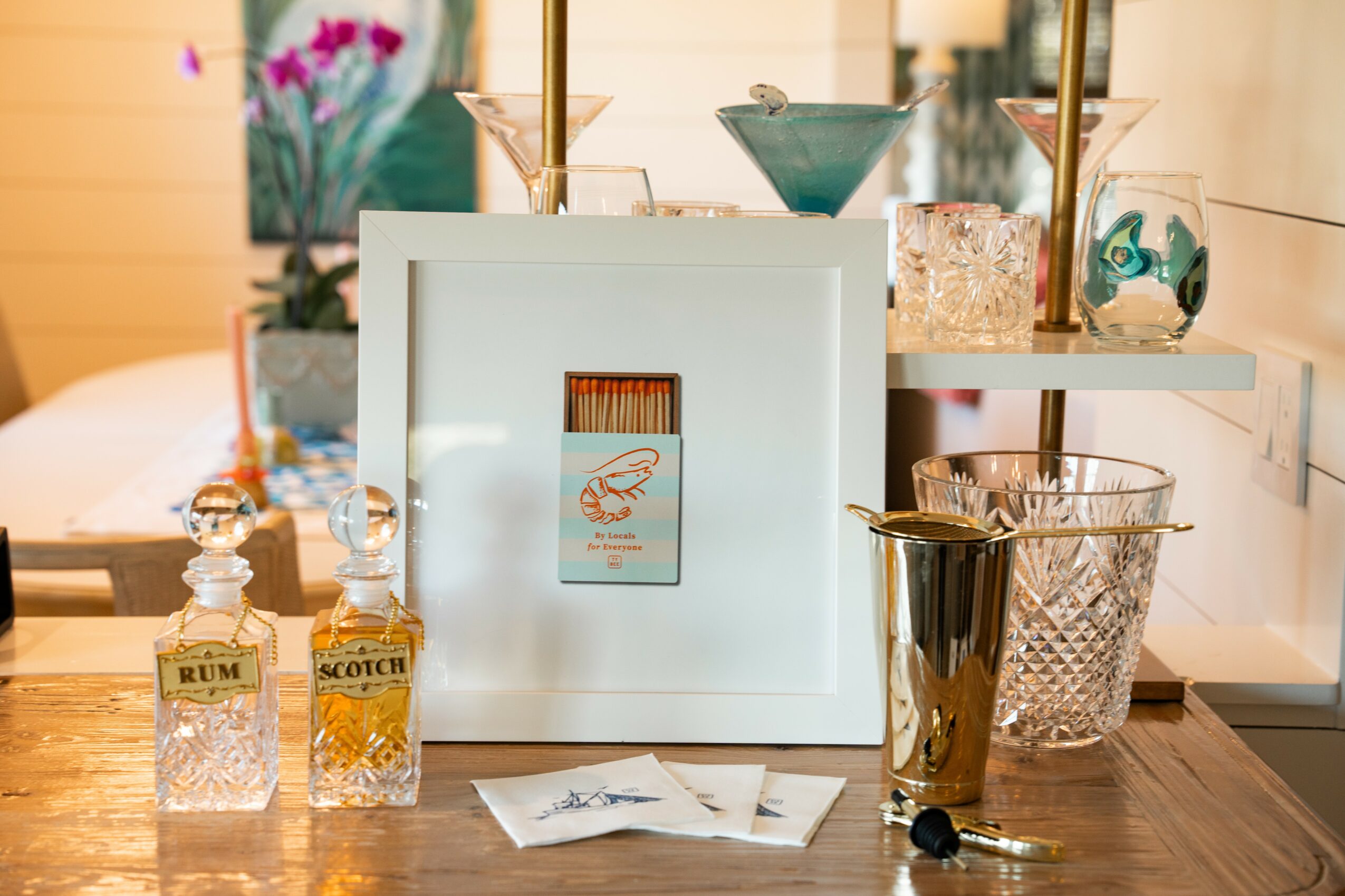 Decorative display with bottles, a framed picture, and various glassware on a wooden table, with a blurred background.