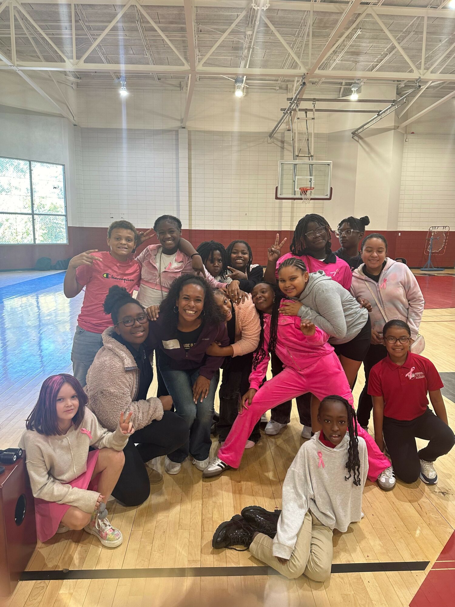 Group of people posing in a gymnasium, some sitting and some standing, with a basketball hoop in the background.