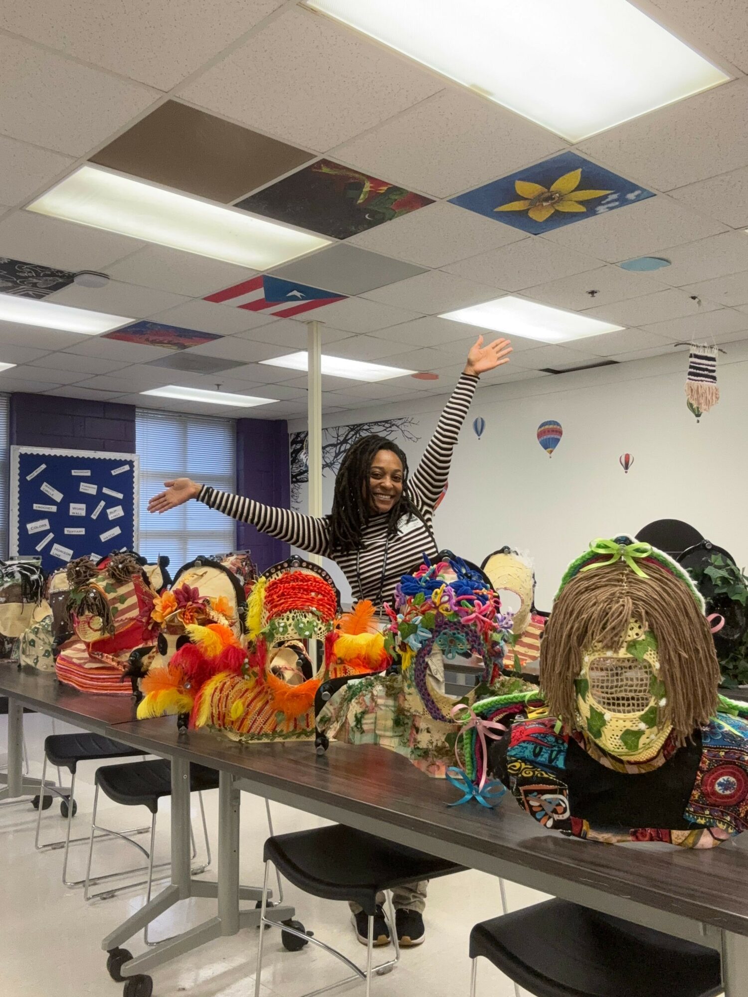 Person with long hair and striped shirt standing behind a table with colorful decorations and plush toys, in a decorated room.