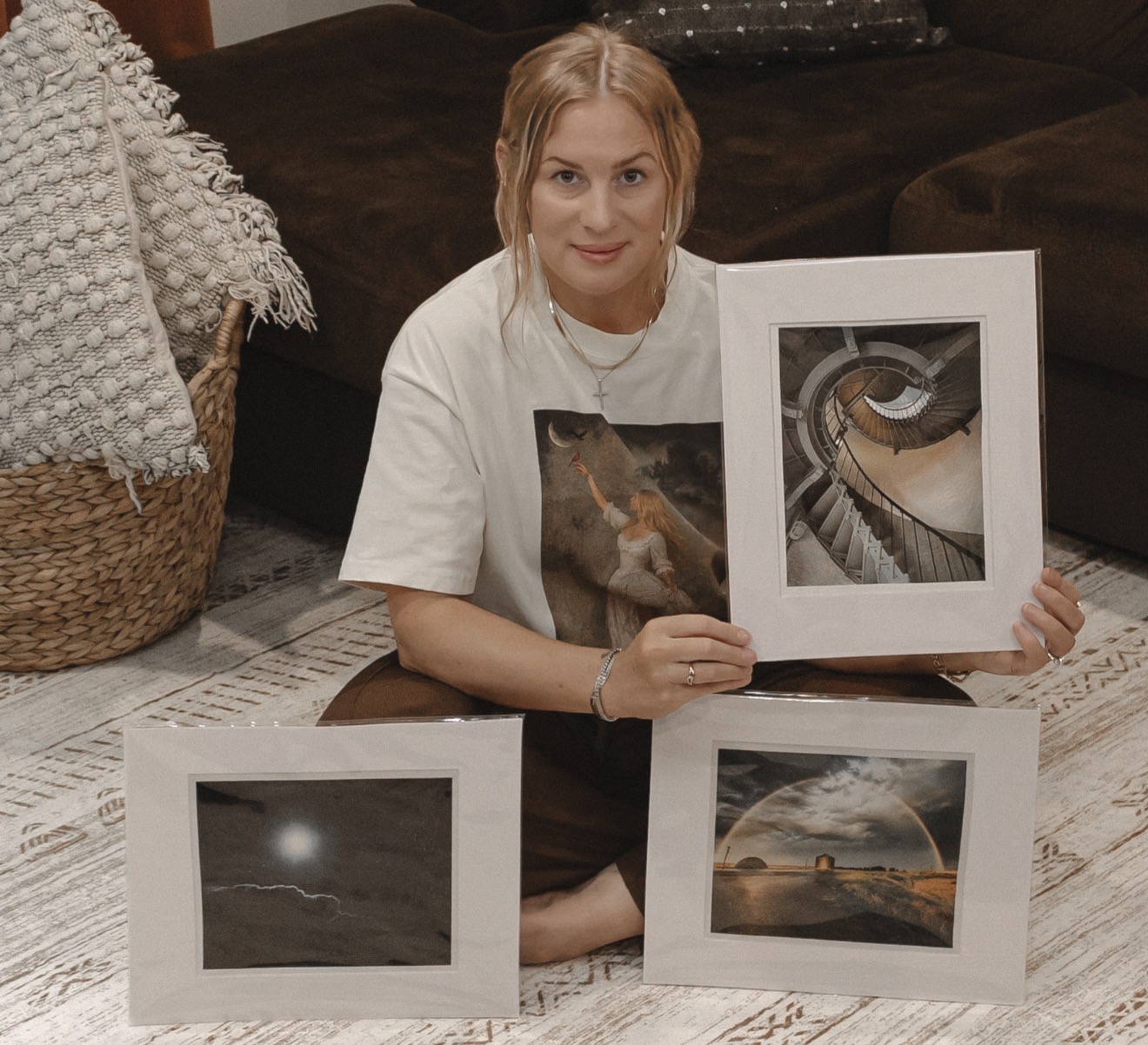 Woman sitting on floor holding framed photographs, with two more photos on the floor, in a cozy room.