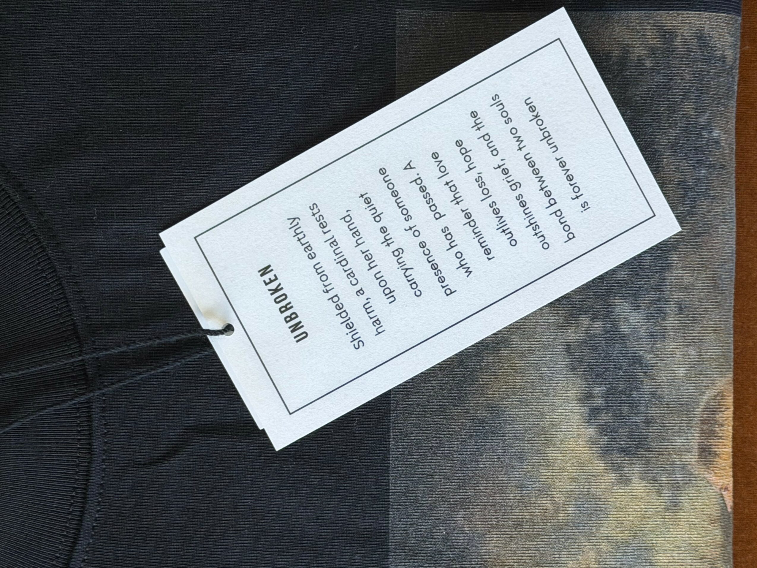 White tag with black text attached to dark fabric, with a background of cloudy sky. Tag contains instructions or information.