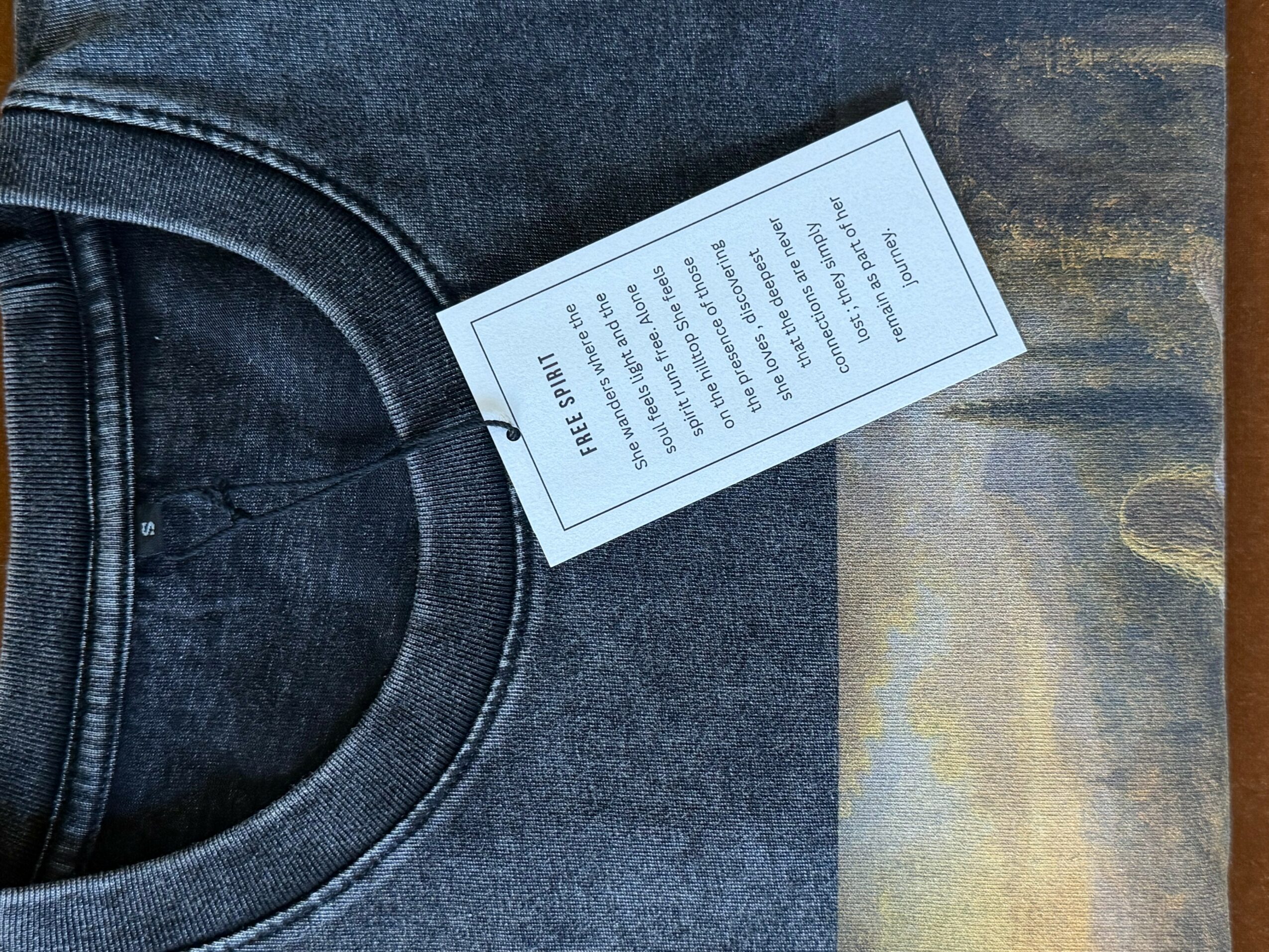 Black denim jeans with a white tag attached, lying on a wooden surface.