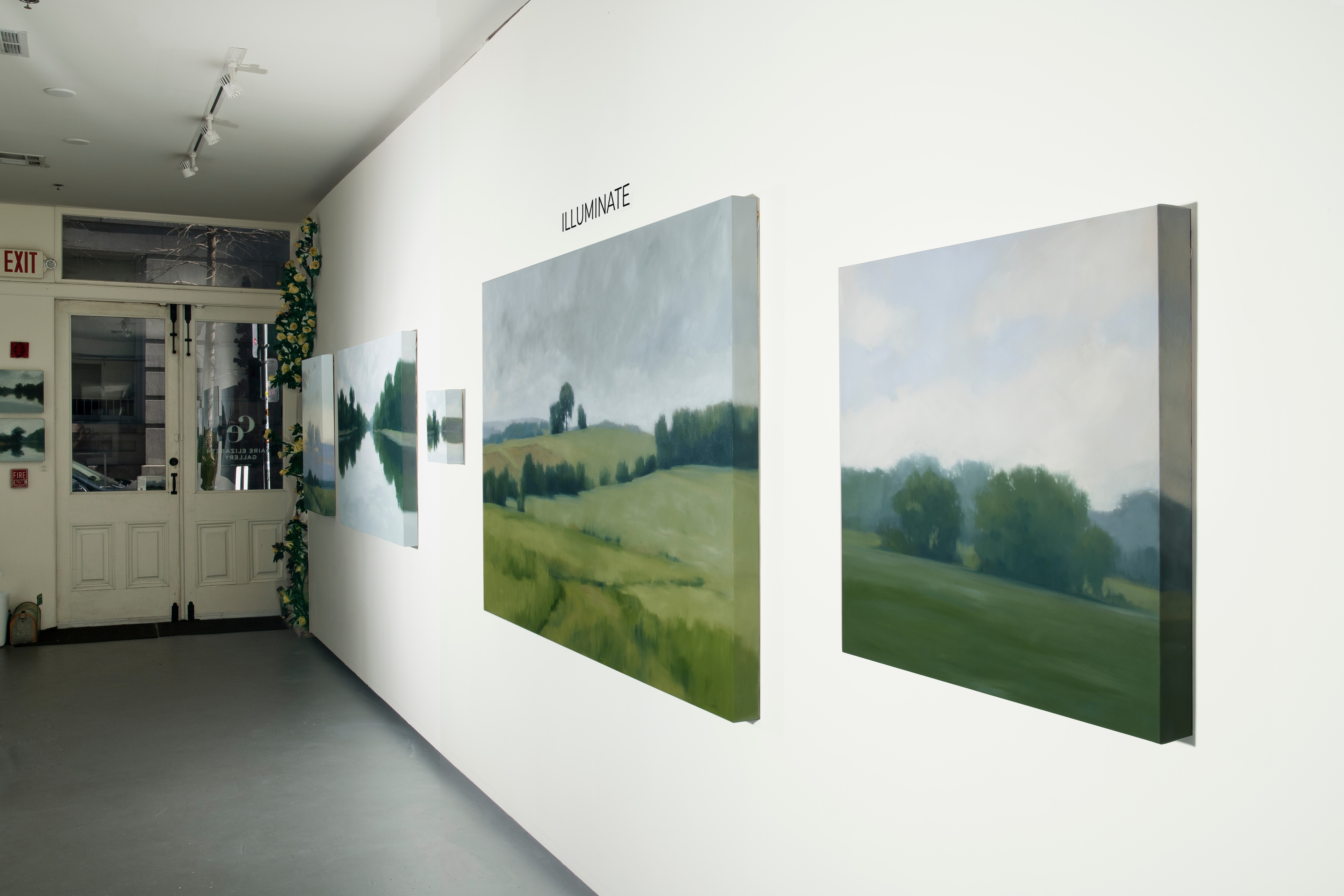 Gallery wall with landscape paintings, white wall, door, and exit sign visible in the background.