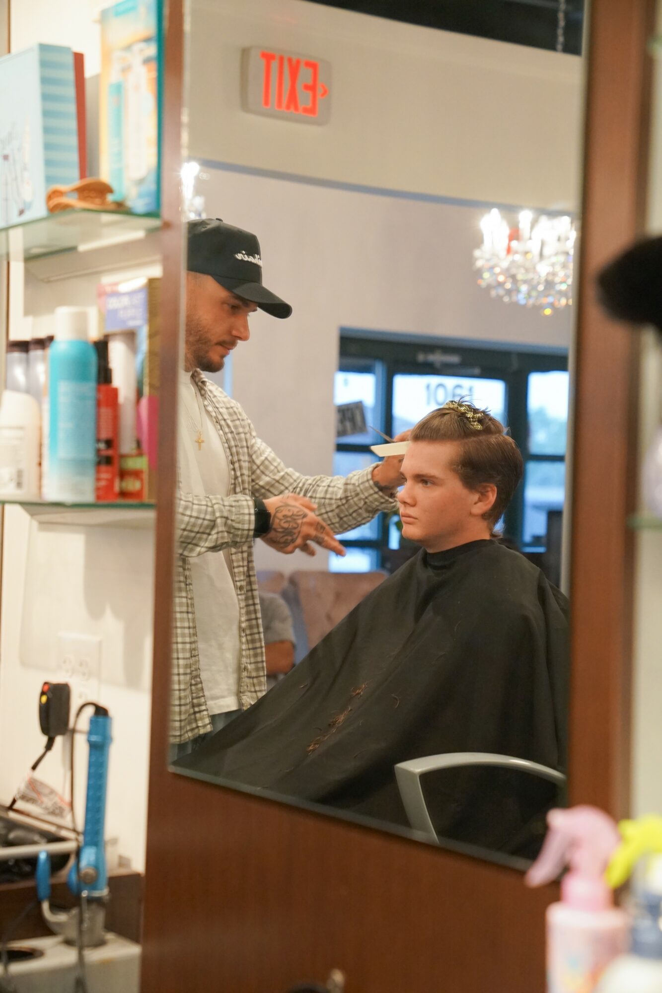 A person getting a haircut in a salon, with a stylist working on their hair, reflected in a mirror.