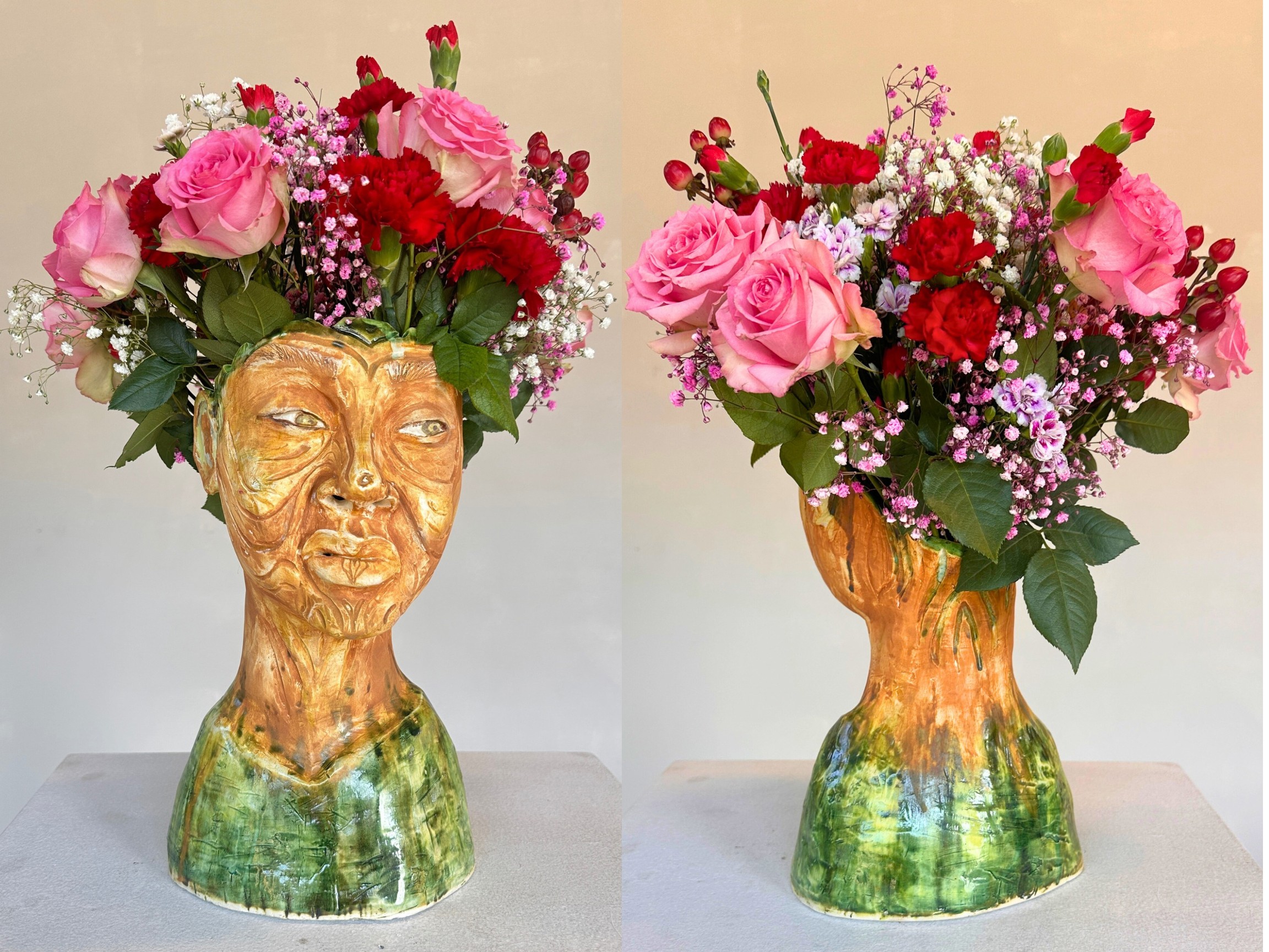 Vase shaped like a human head with a floral arrangement of pink and red flowers on top.