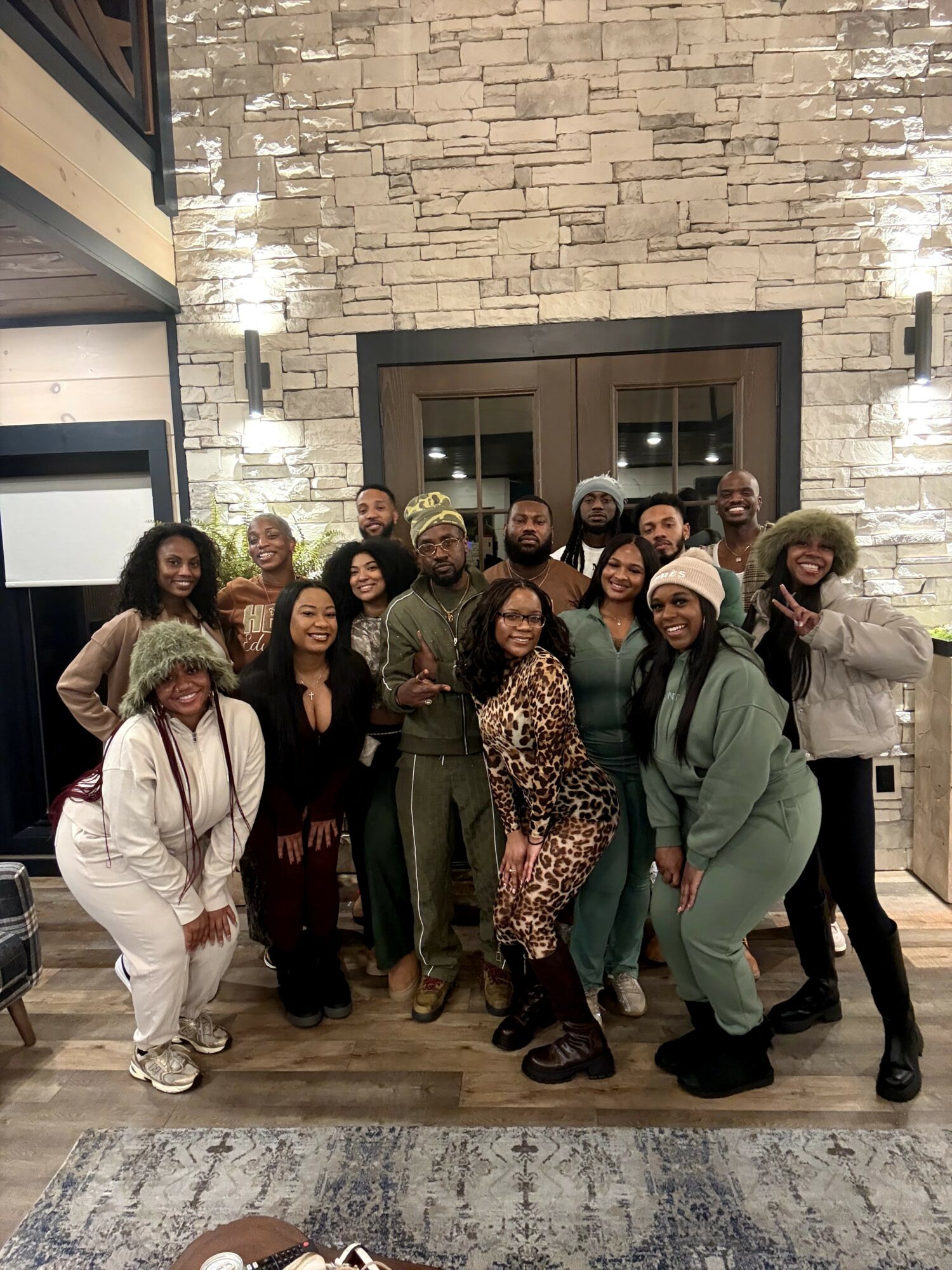 Group of people posing indoors in front of a stone wall and glass door, smiling and dressed casually.
