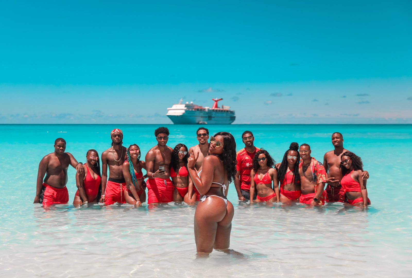 Group of people in red swimsuits standing in clear ocean water with a cruise ship in the background.