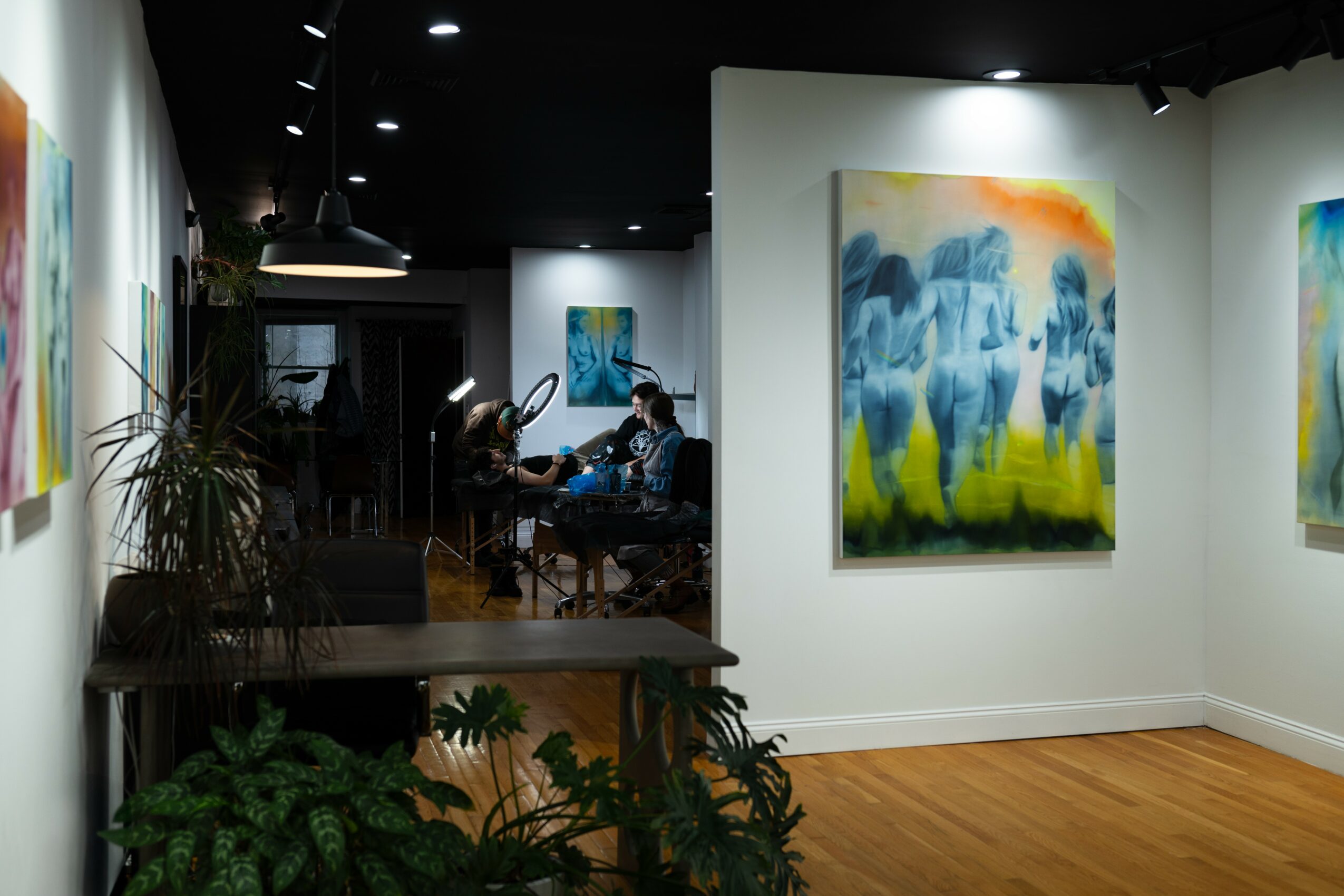People sitting at a table in an art gallery with colorful paintings on white walls and wooden flooring.