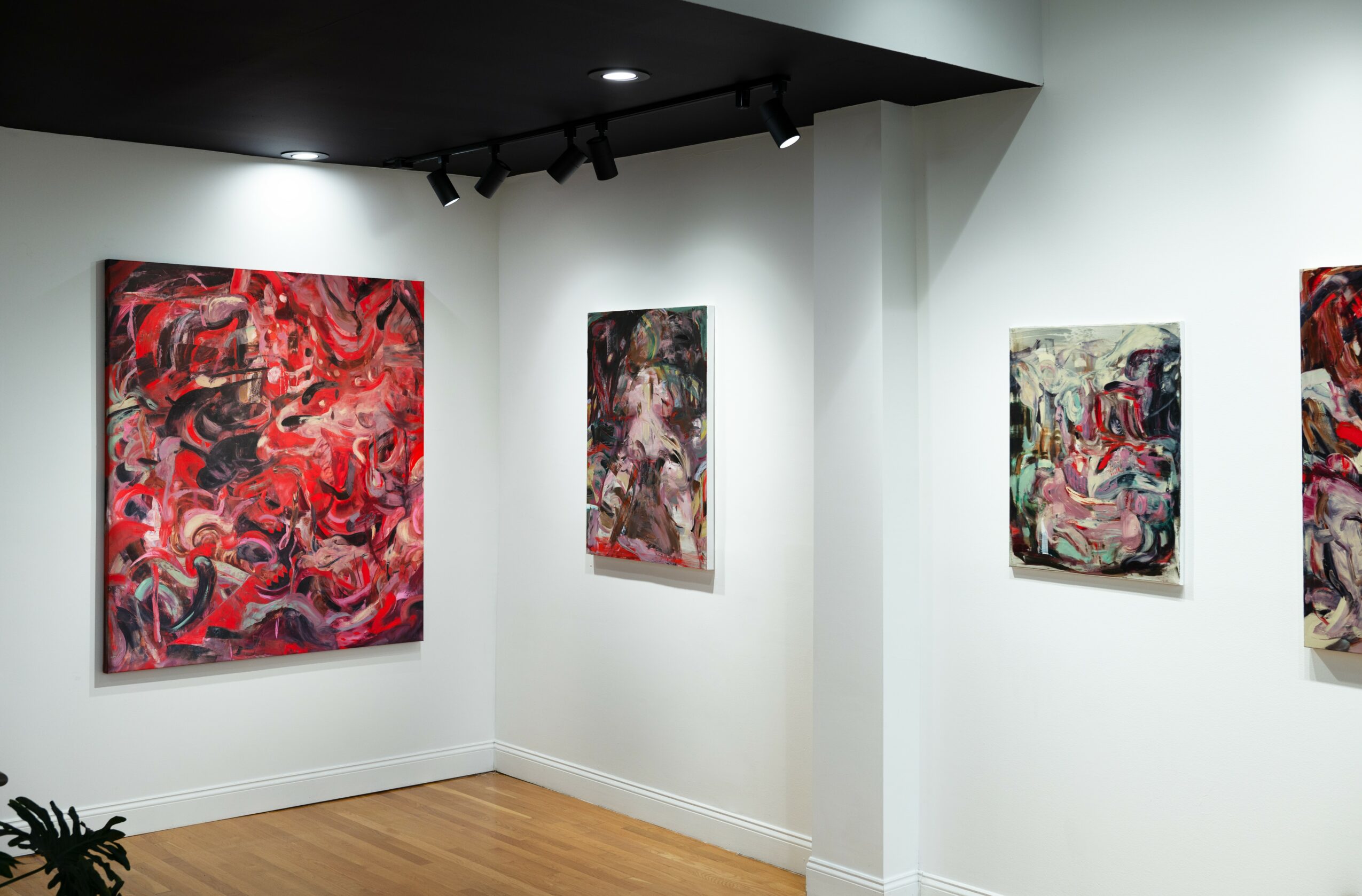 Gallery with four abstract paintings on white walls, wooden floor, and black ceiling lights.