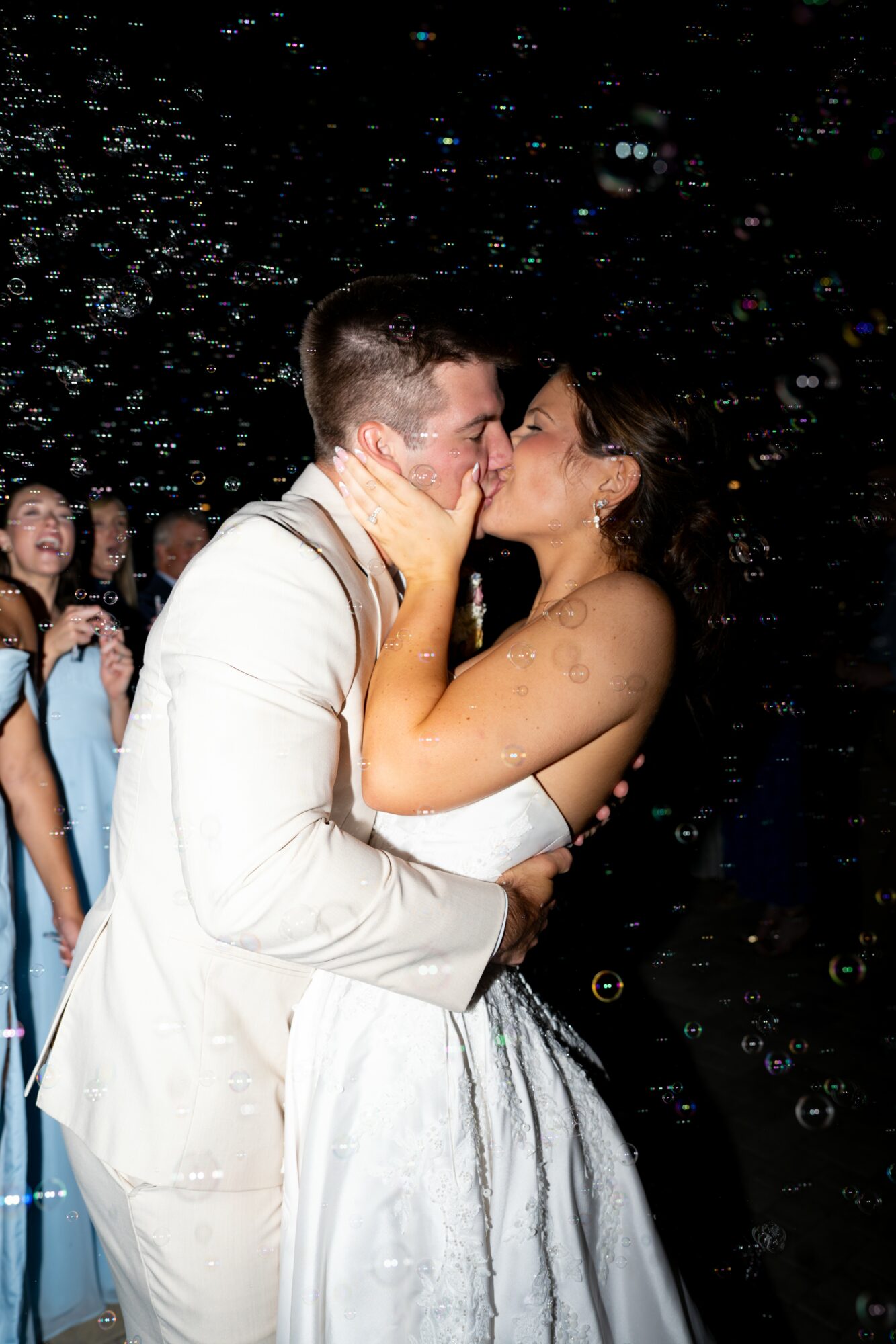 Couple kissing at a celebration, with people and confetti in the background.