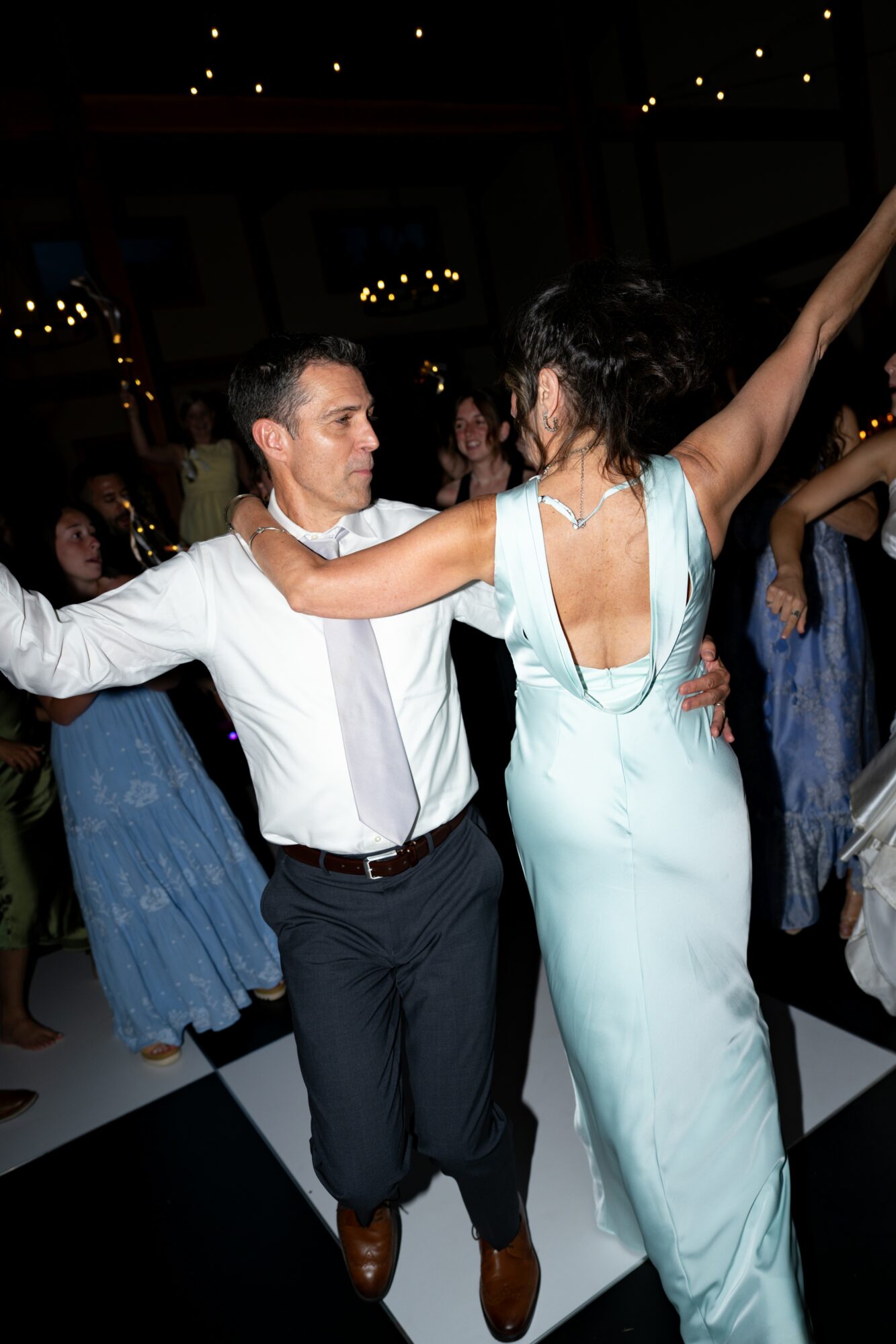 Couple dancing at a formal event, woman in a light blue gown and man in a white shirt and dark pants, surrounded by other dancers.