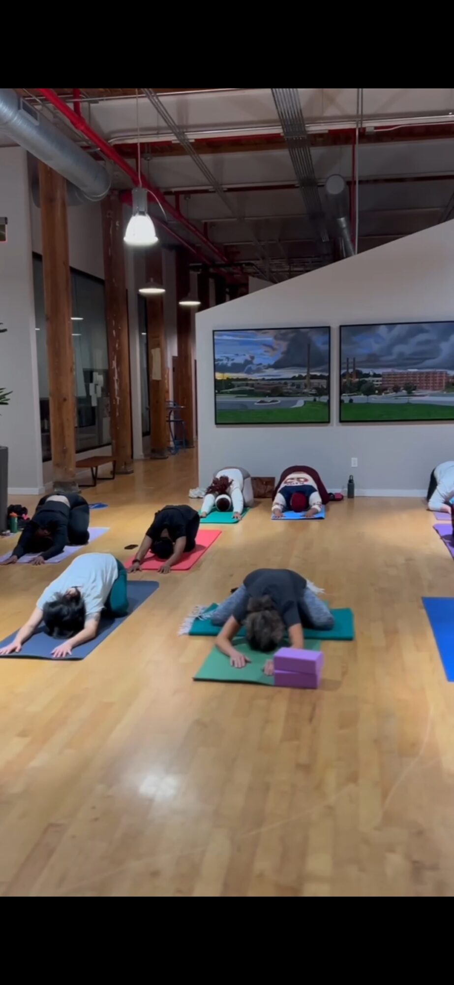 People practicing yoga on mats in a spacious indoor studio with large screens and wooden floors.