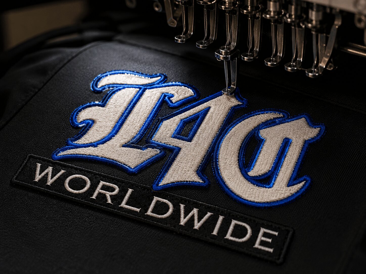 Close-up of embroidery with the words 'TAG' in blue and white, and 'WORLDWIDE' in white on black fabric.