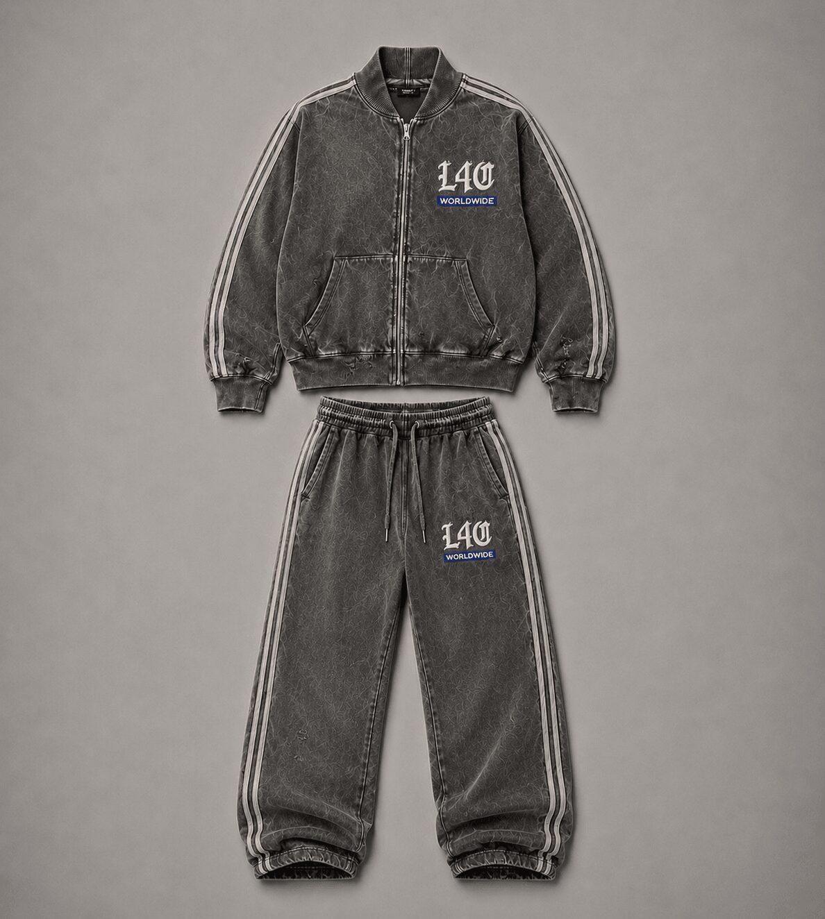 Gray tracksuit with zip-up jacket and matching pants, both featuring white stripes and blue embroidered text, on a gray background.