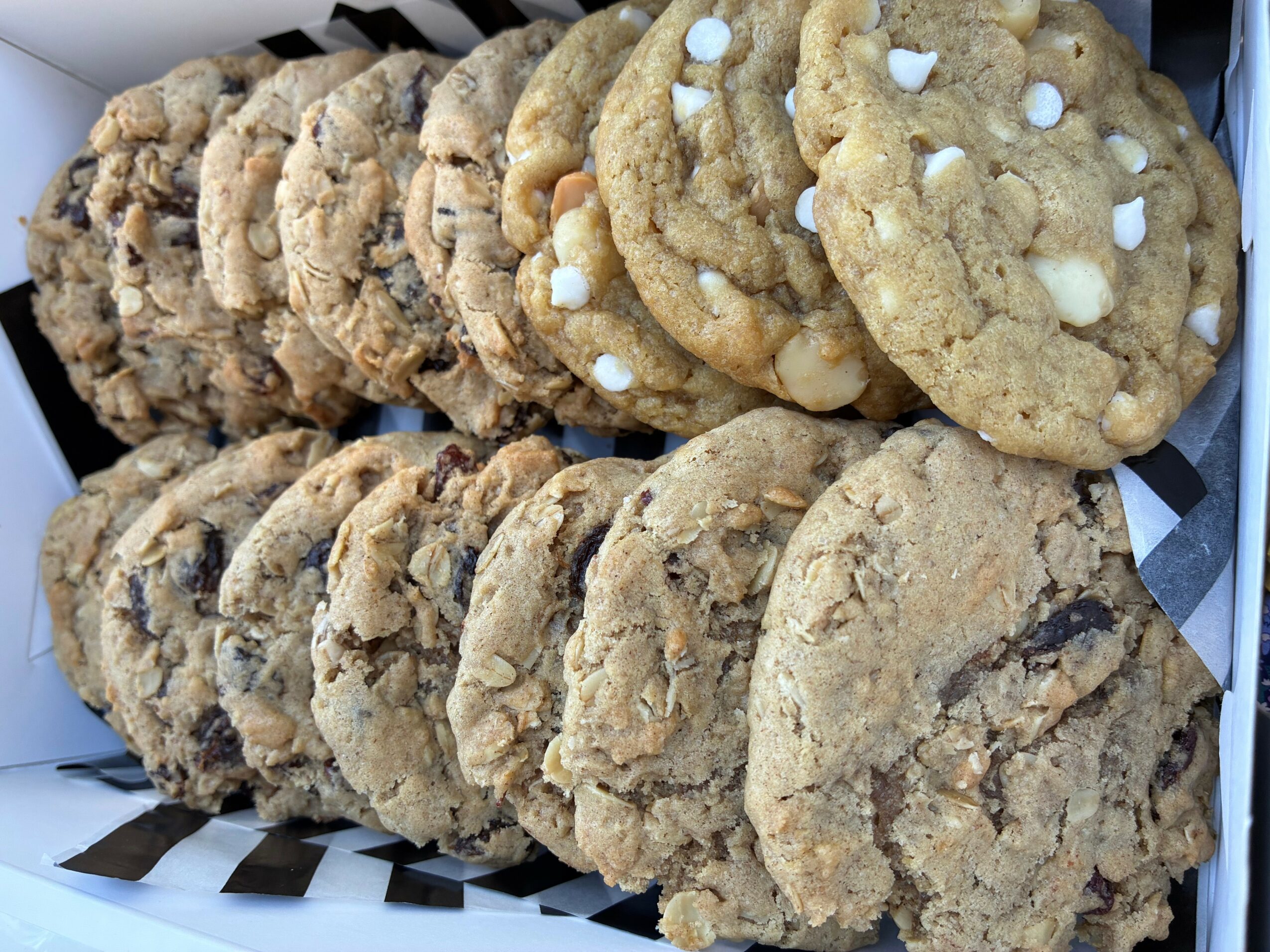 Stack of chocolate chip and white chocolate cookies in a basket, some with white chocolate chips, on black and white paper.
