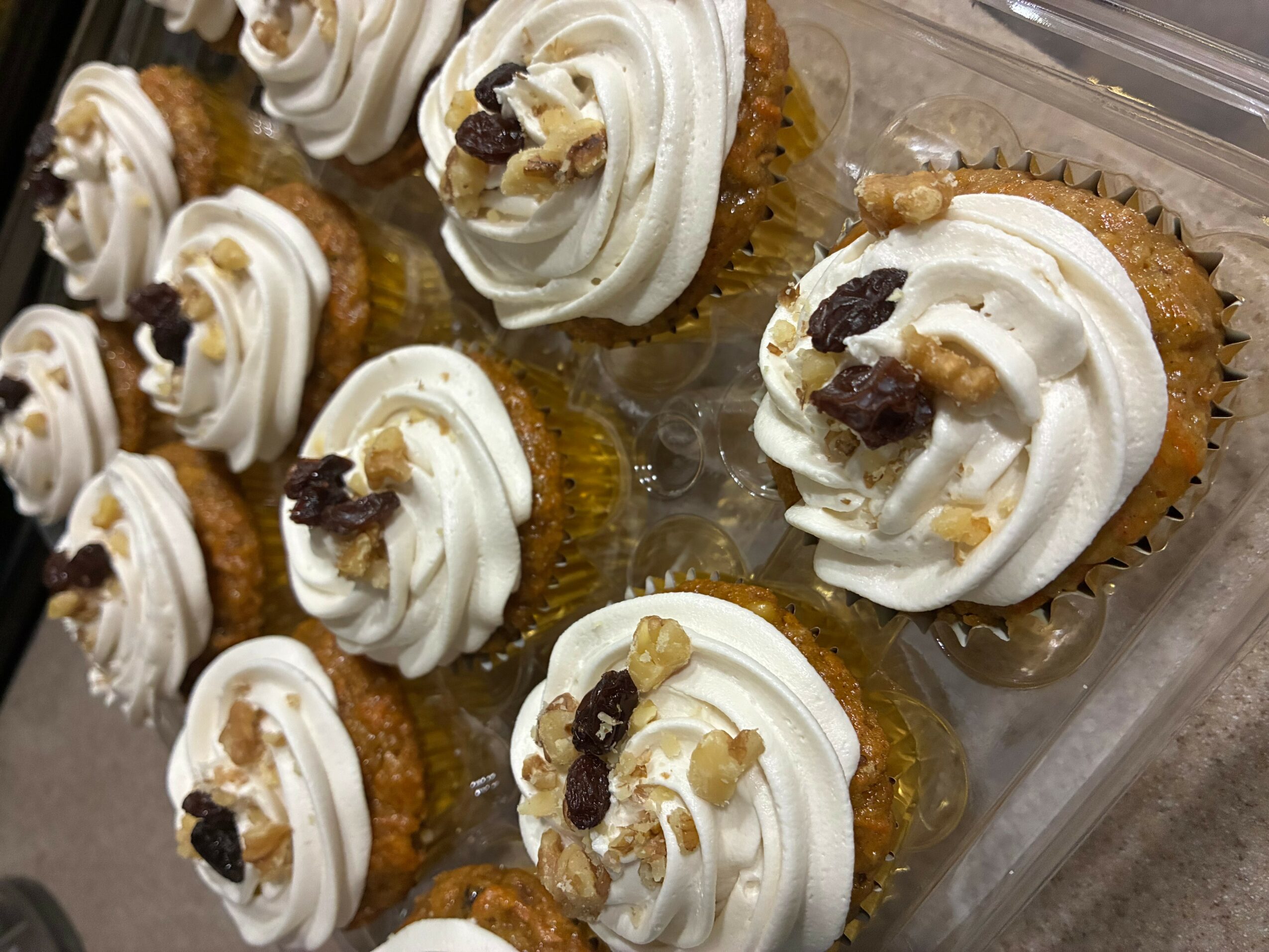 Cupcakes with white frosting and toppings in a plastic container, viewed from above.