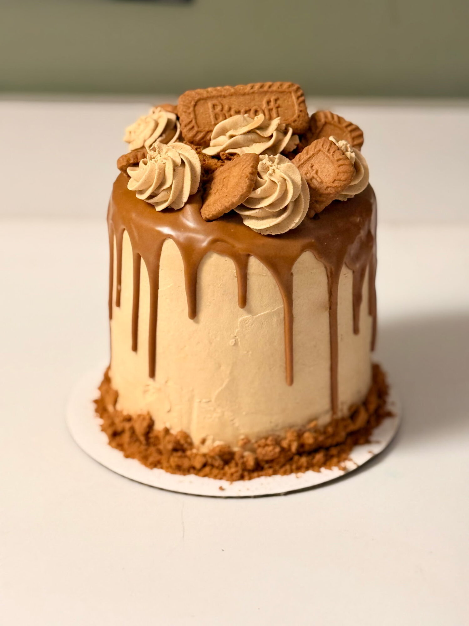 Small cake with caramel drizzle, topped with whipped cream, cookies, and biscuits, on a white surface.