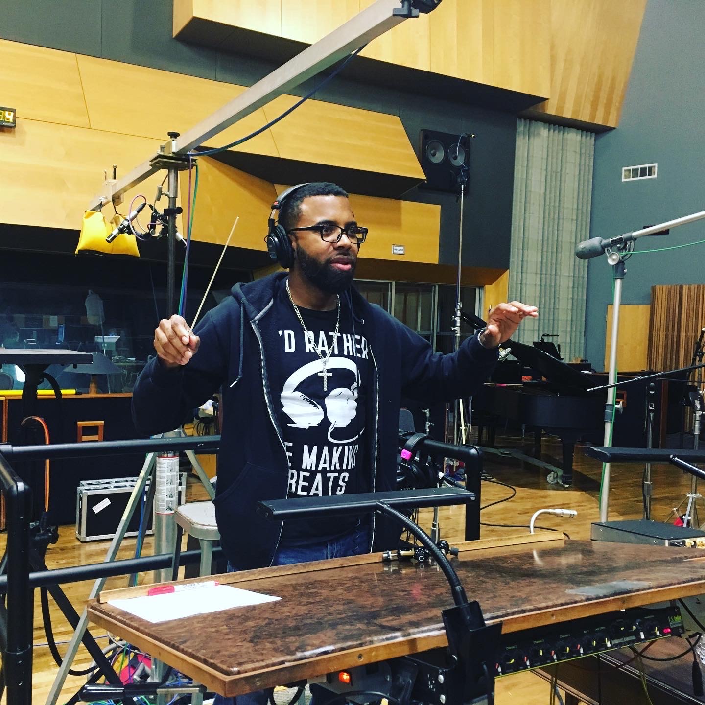 Person with headphones conducting in a recording studio, surrounded by microphones and equipment.